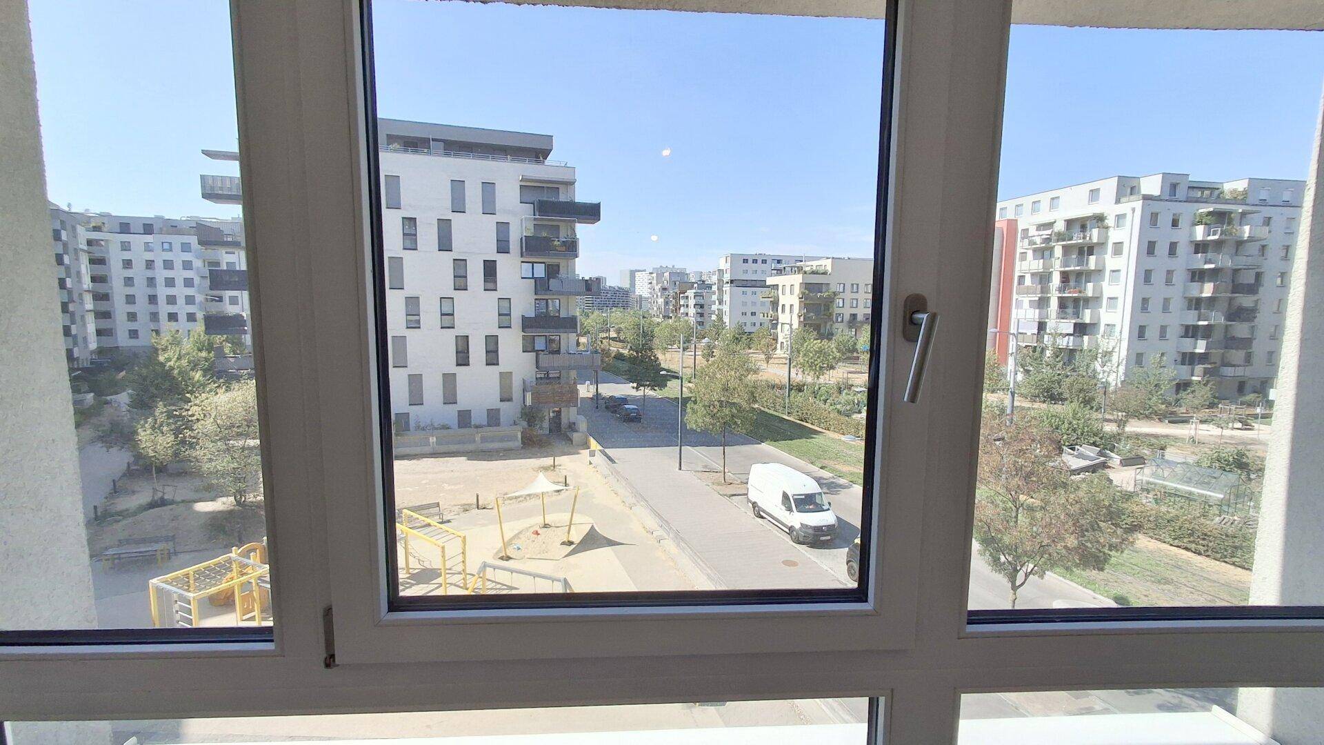 Blick aus dem Fenster auf einen Spielplatz, eine Straße und moderne Wohngebäude in der Umgebung.