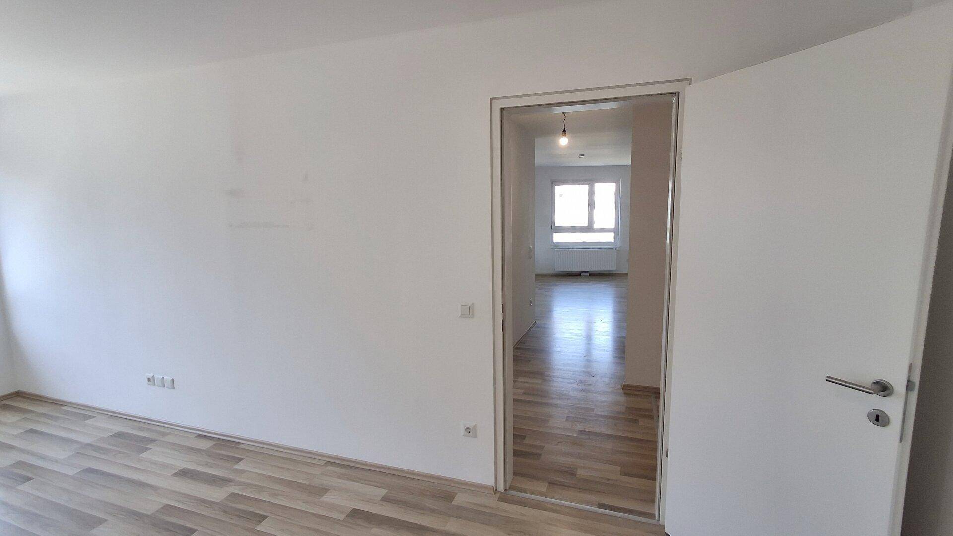 Helles Zimmer mit Laminatboden und Zugang zu einem weiteren Raum, ideal für flexible Nutzung.