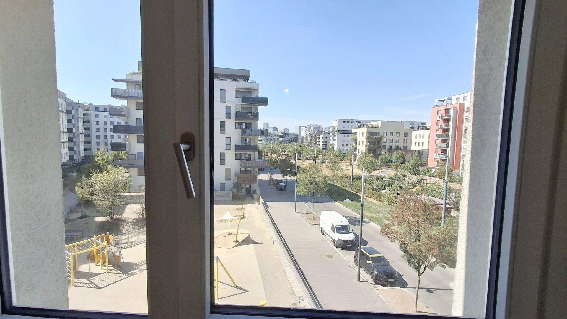 Blick aus dem Fenster auf einen Spielplatz, eine Straße und moderne Wohngebäude in der Umgebung.