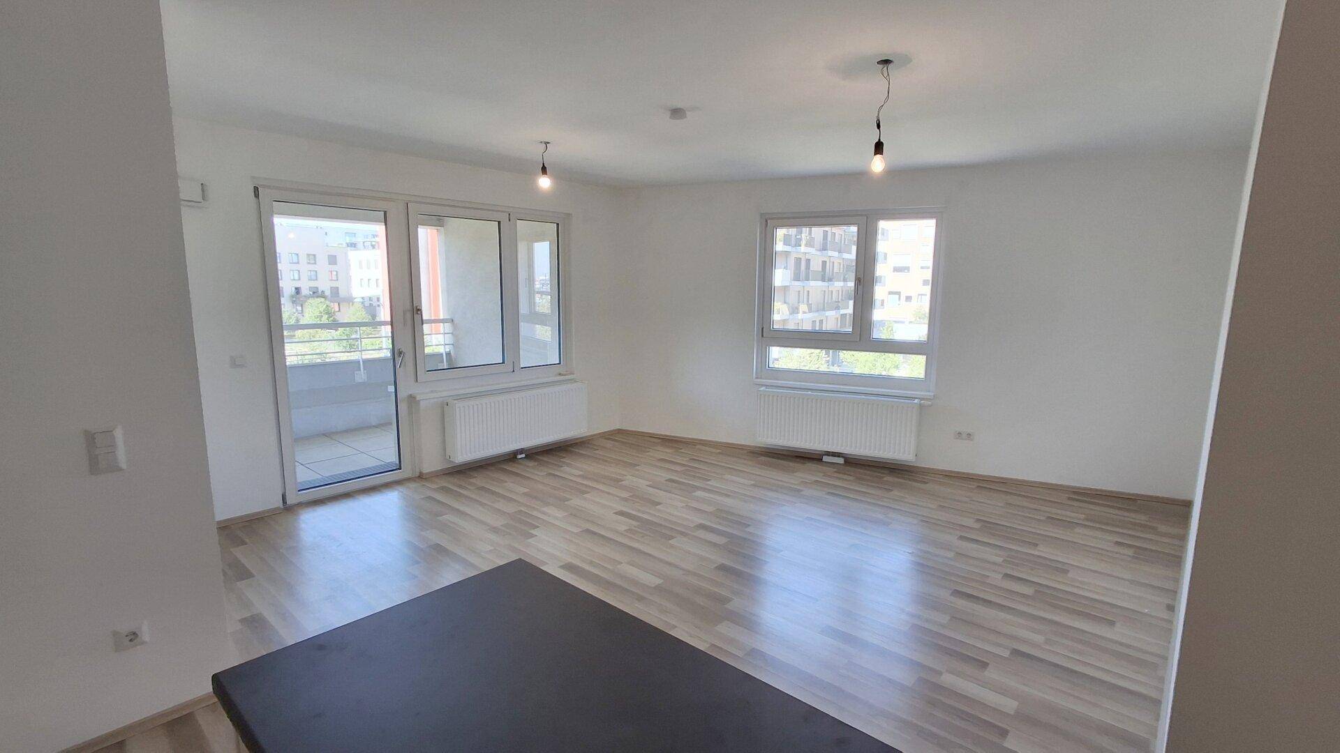 Helles Wohnzimmer mit Laminatboden, großen Fenstern und direktem Zugang zum Balkon.