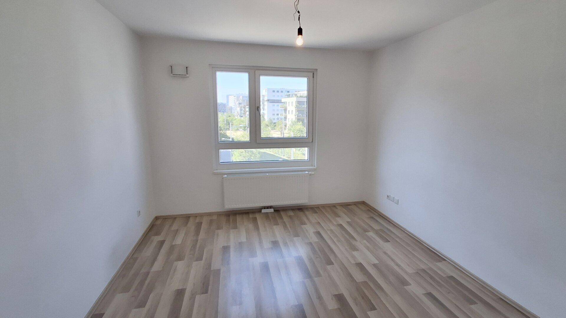 Freundliches Zimmer mit Laminatboden und großem Fenster, das viel Tageslicht hereinlässt.