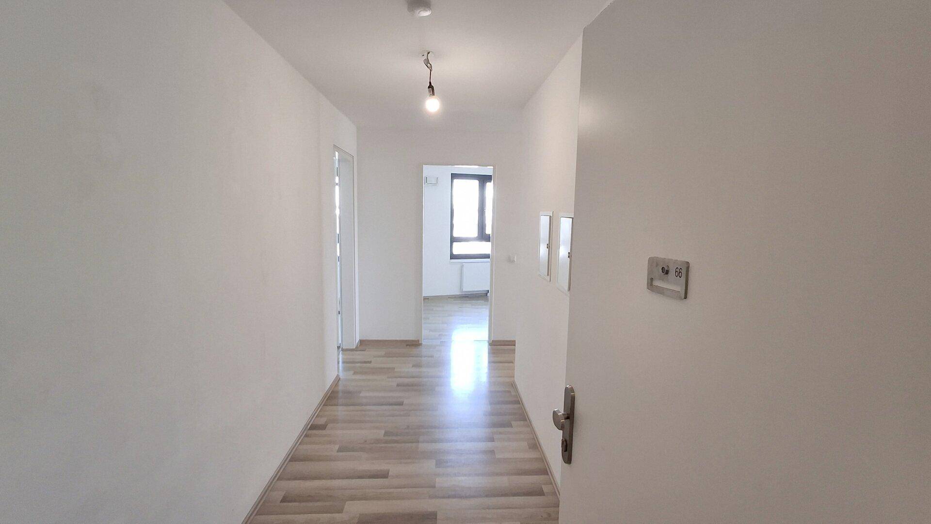 Heller Flur mit Laminatboden und weiß gestrichenen Wänden, der zu weiteren Räumen führt.