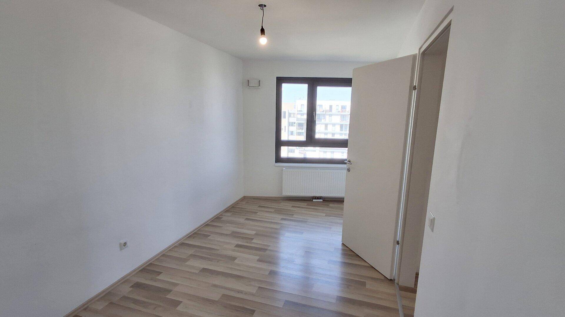 Leerer Raum mit Laminatboden und großem Fenster, das viel Tageslicht hereinlässt.