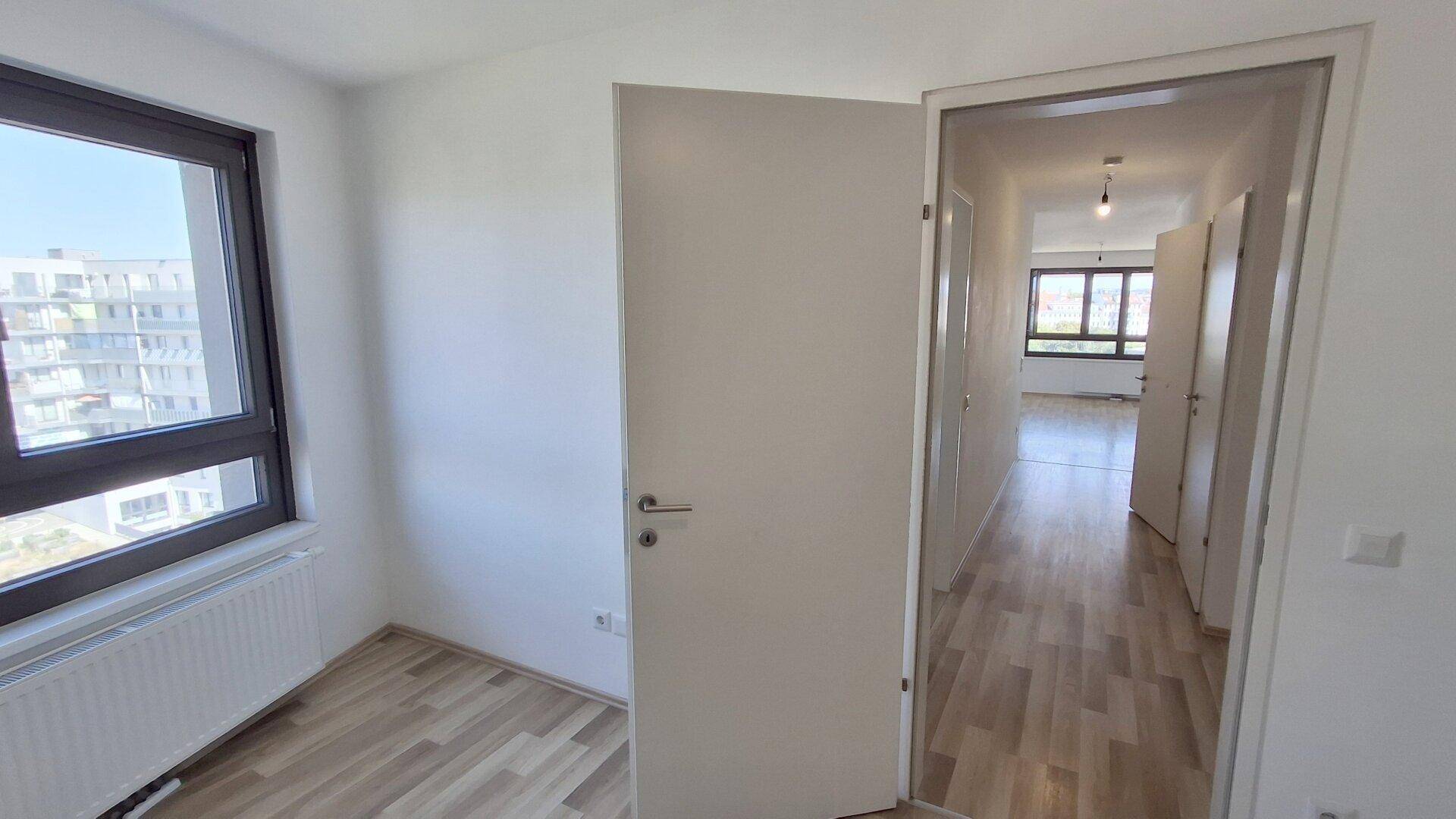 Heller Raum mit Laminatboden und Fenster, das den Blick auf die umliegenden Gebäude freigibt.