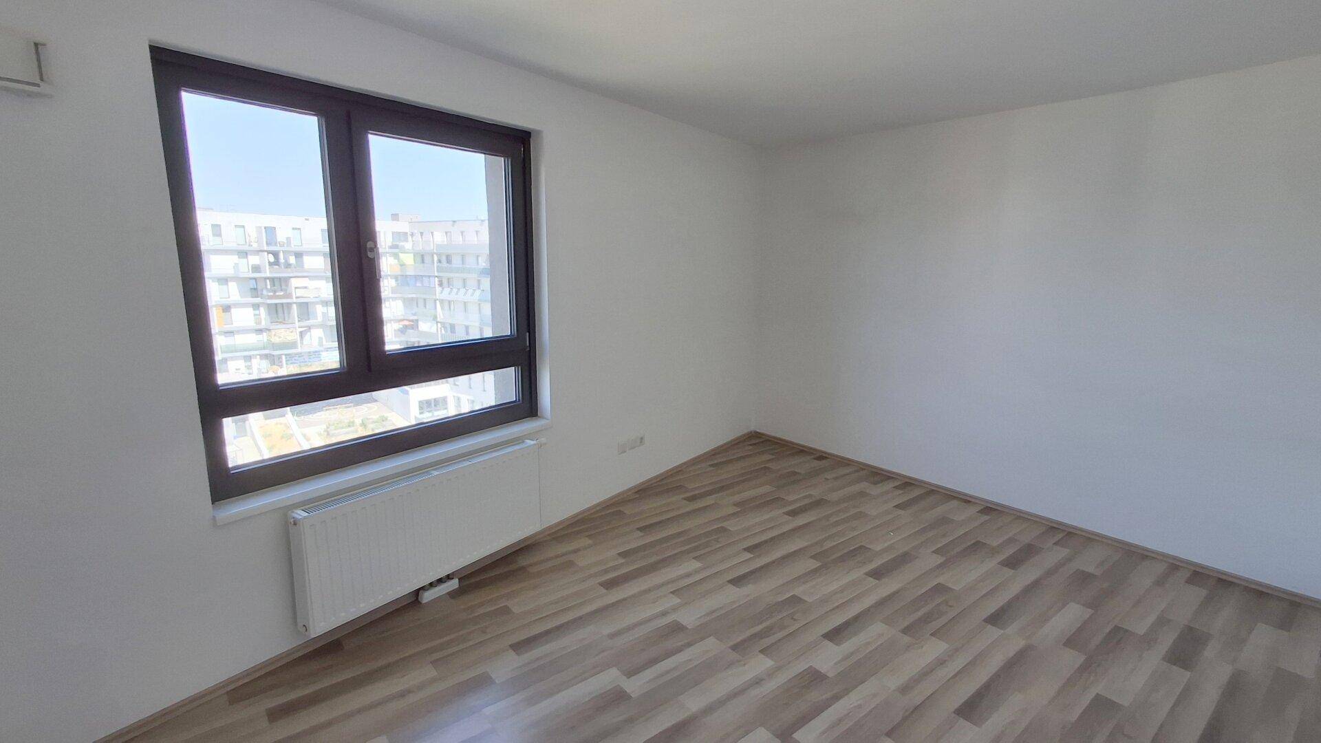 Geräumiger, leerer Raum mit Laminatboden und großem Fenster, das viel Helligkeit bietet.