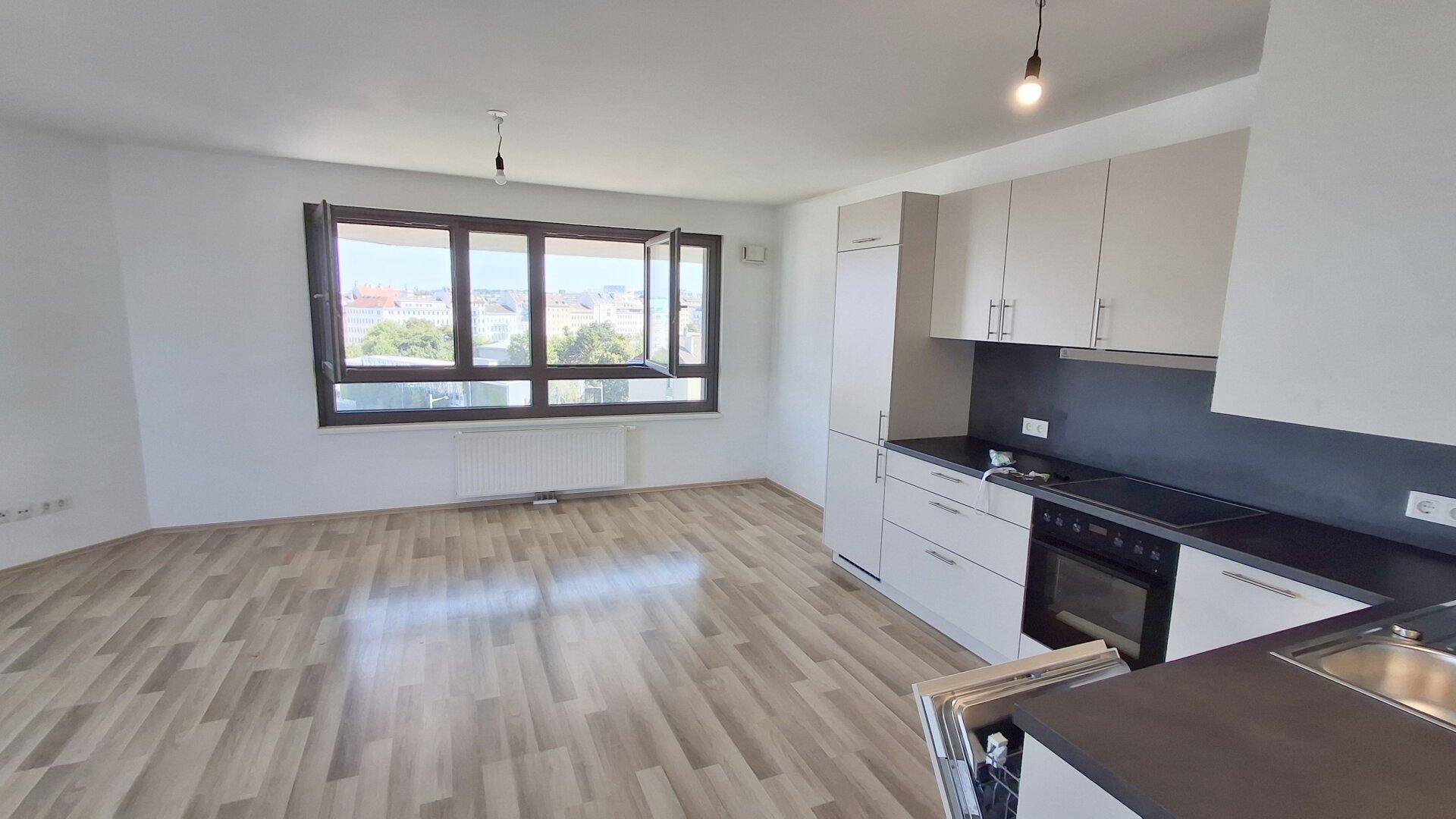 Offener Wohnbereich mit integrierter Küche, Laminatboden und großen Fenstern mit Stadtblick.