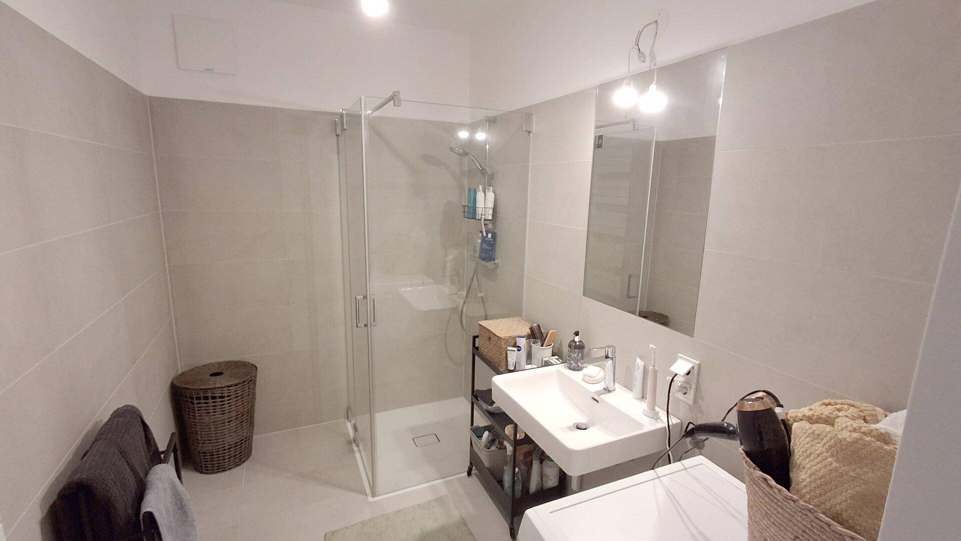Modernes Badezimmer mit begehbarer Dusche, großformatigen Fliesen und einem Waschbecken.