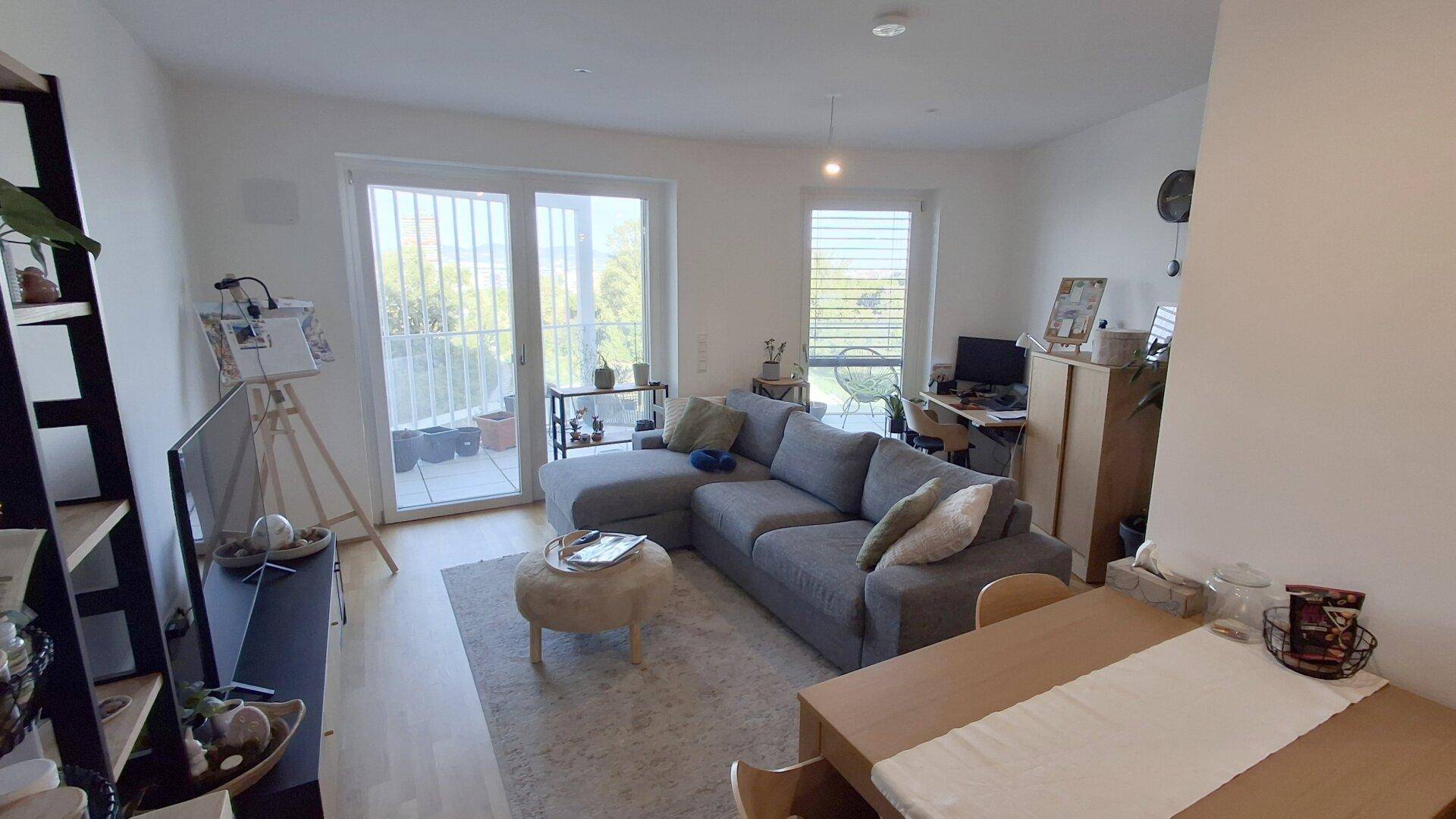 Heller Wohnbereich mit großem Sofa, Holzboden und Zugang zu einem Balkon.