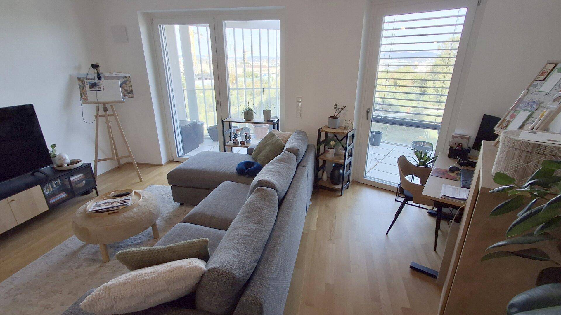 Gemütlicher Wohnbereich mit Sofa, Holzboden und großen Fenstern mit Blick ins Grüne.
