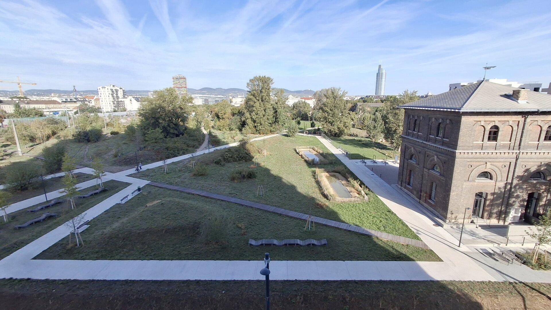 Weitläufige Parkanlage mit Wegen, Grünflächen und einem historischen Gebäude im Hintergrund.