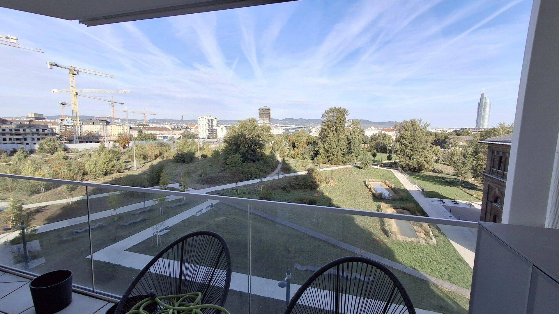 Balkon mit Glasgeländer bietet einen weiten Blick auf eine grüne Parklandschaft und die Stadt.