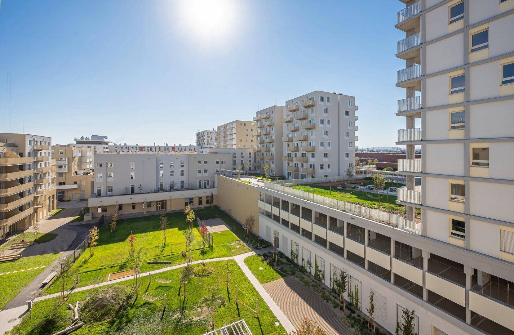 Sonniger Überblick über die moderne Wohnanlage mit ihren Grünflächen und umliegenden Gebäuden.