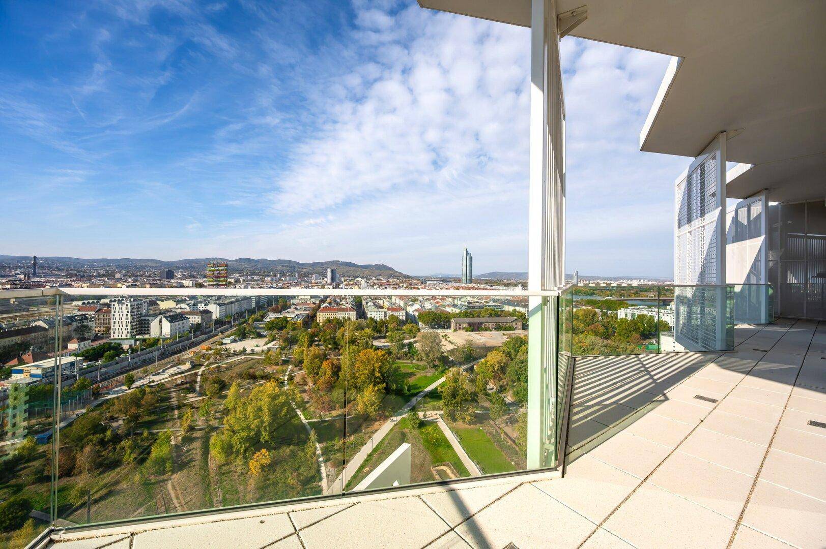 Weitläufige Terrasse mit Glasgeländer bietet einen beeindruckenden Panoramablick über die Stadt und grüne Flächen.