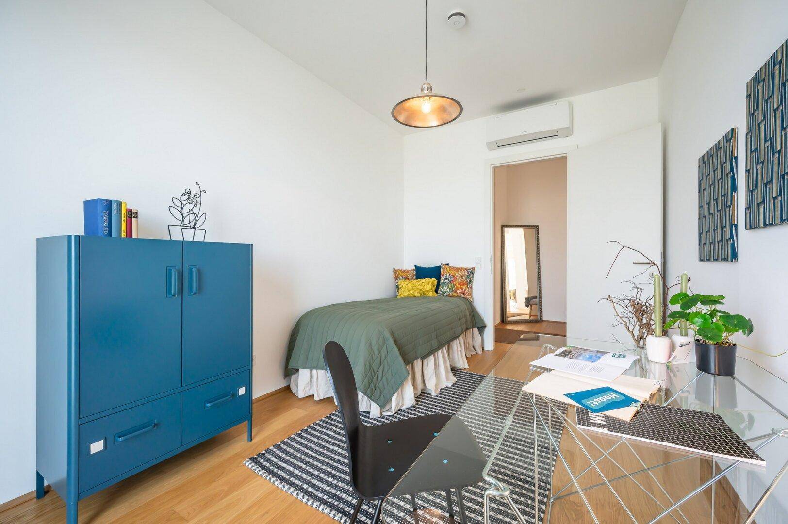 Modernes Schlafzimmer mit Einzelbett, Schreibtisch und blauer Kommode.