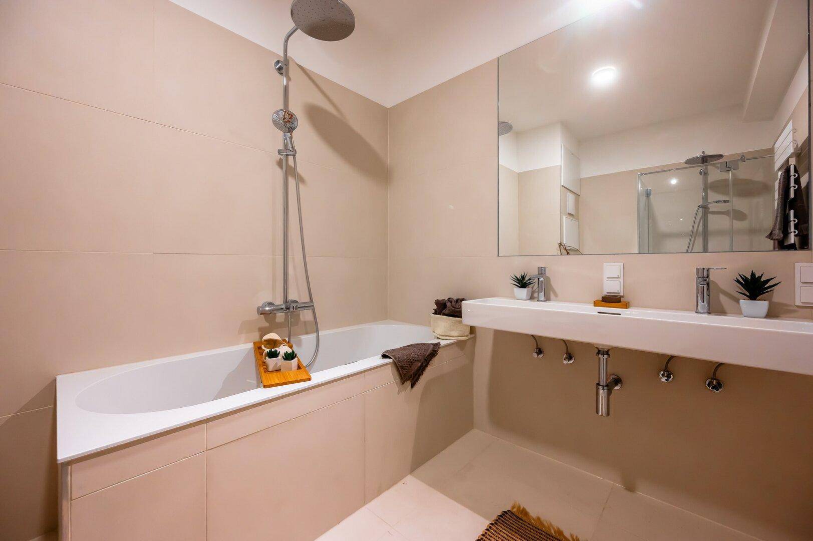 Helles Badezimmer mit Badewanne, Duschkopf und großem Spiegel über dem Waschbecken.