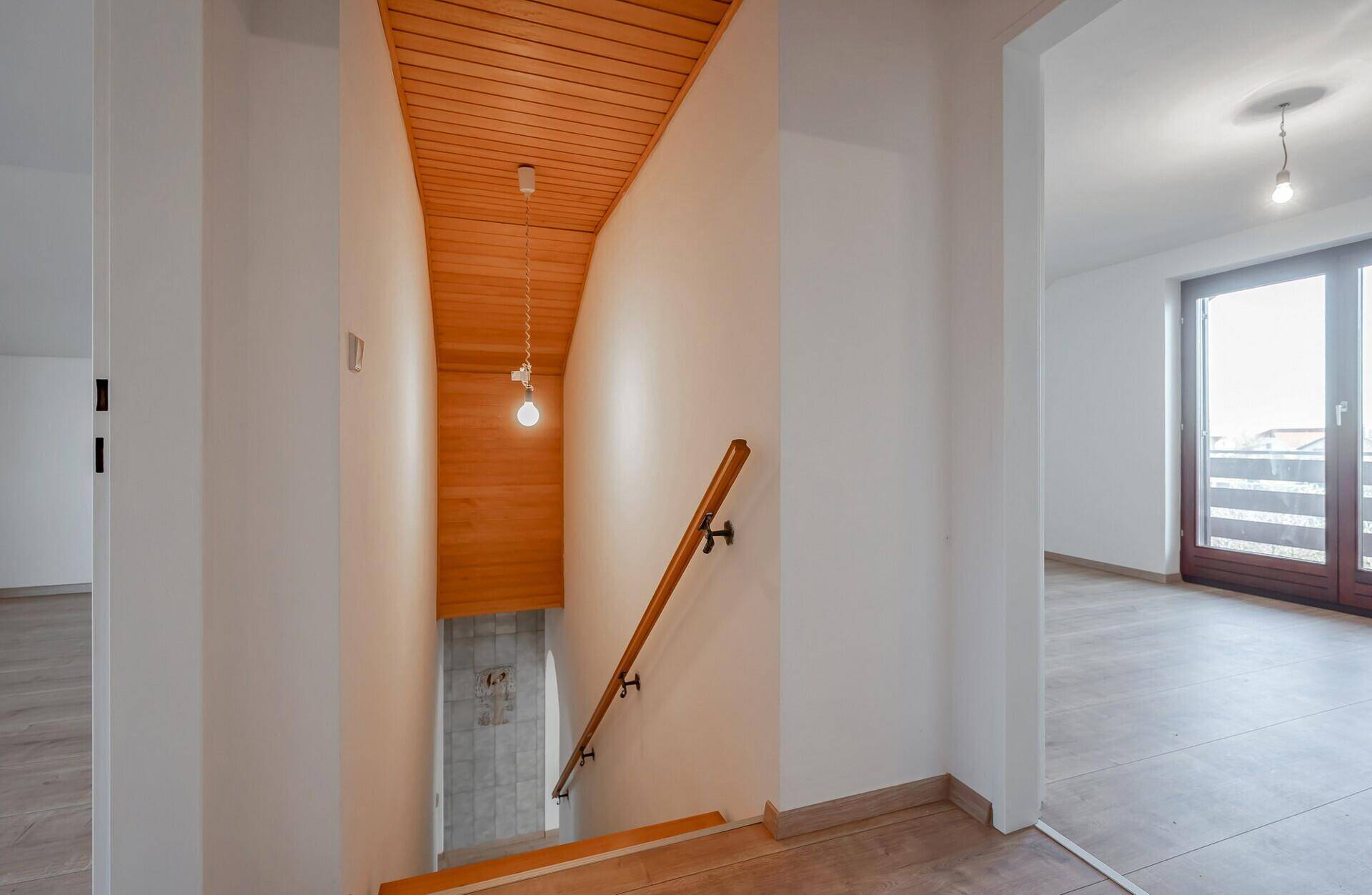 Heller Treppenaufgang mit Holzdecke und Geländer, führt zu einem weiteren Raum mit Balkonzugang.