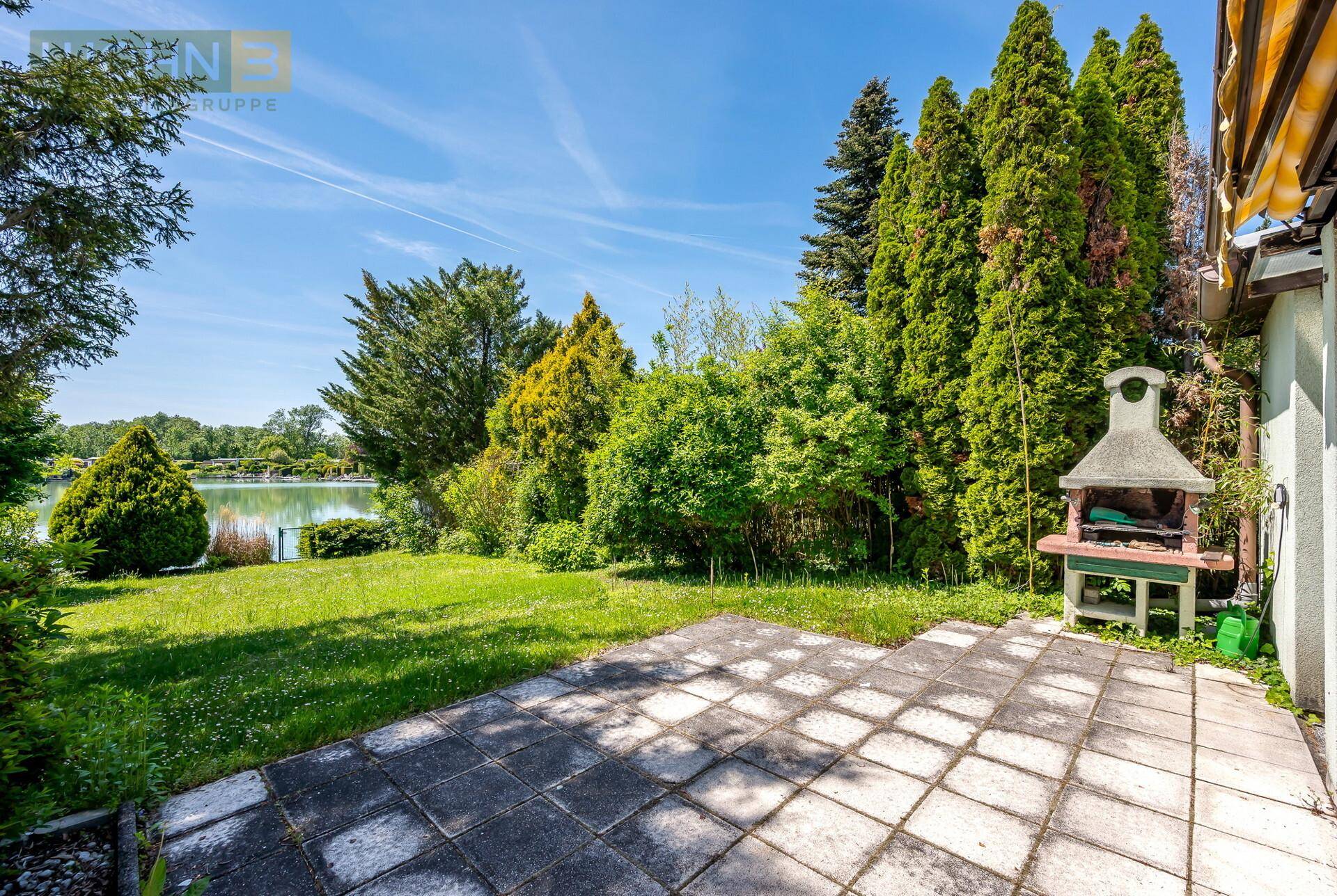 Terrasse mit festem Grill und weitem Blick über den Rasen zum See.