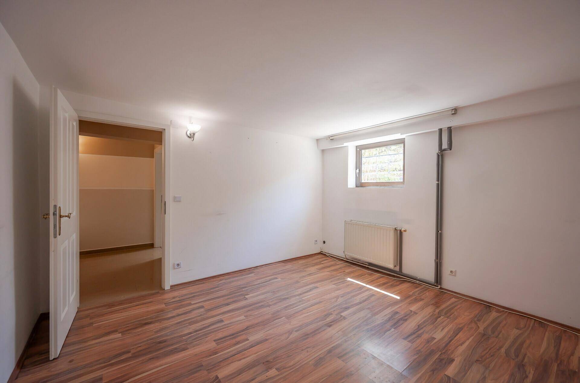 Geräumiges Zimmer im Untergeschoss mit Laminatboden und Heizkörper.
