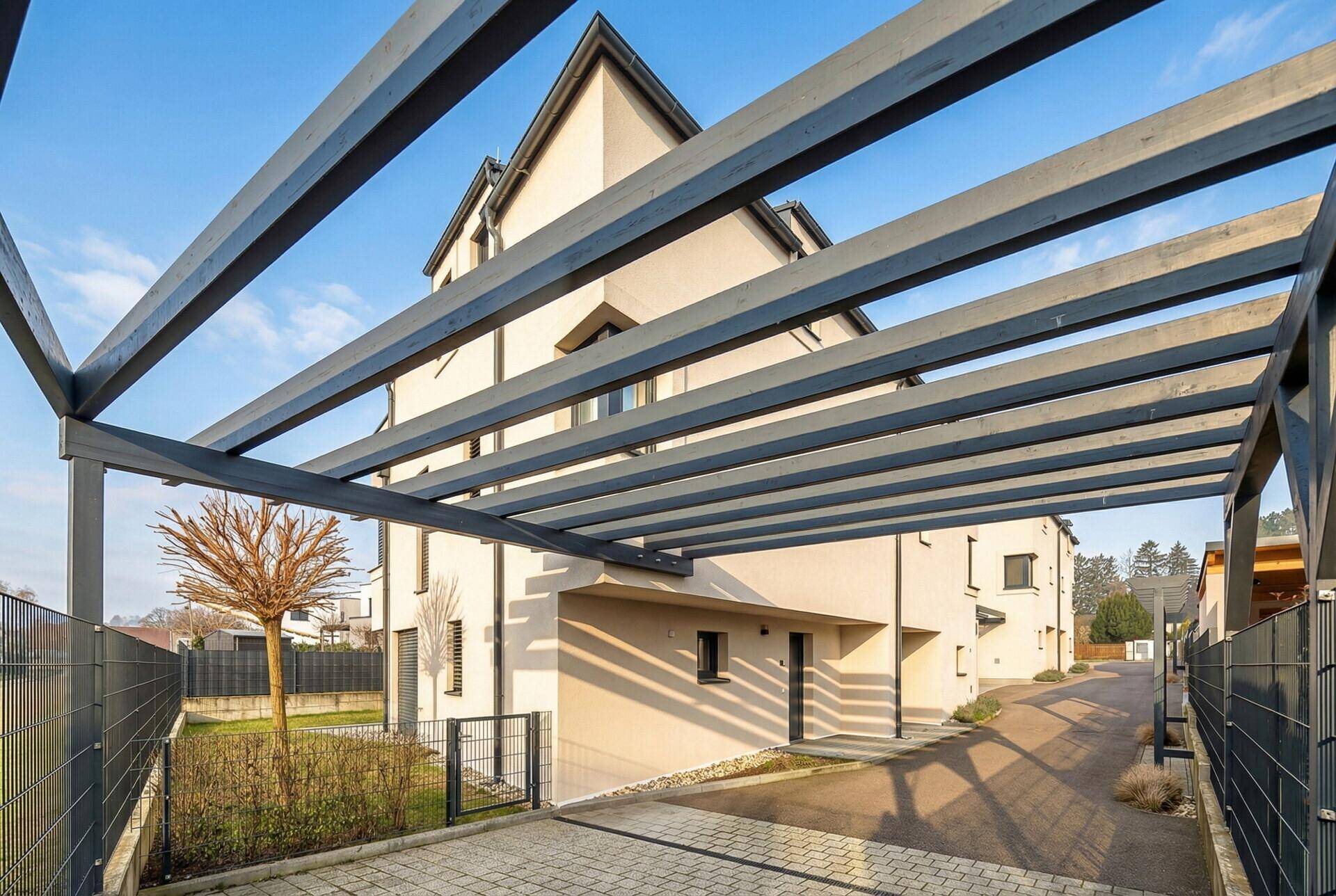 Ansicht des modernen Reihenhauses mit Carport-Struktur und gepflegter Außenanlage bei Sonnenschein.
