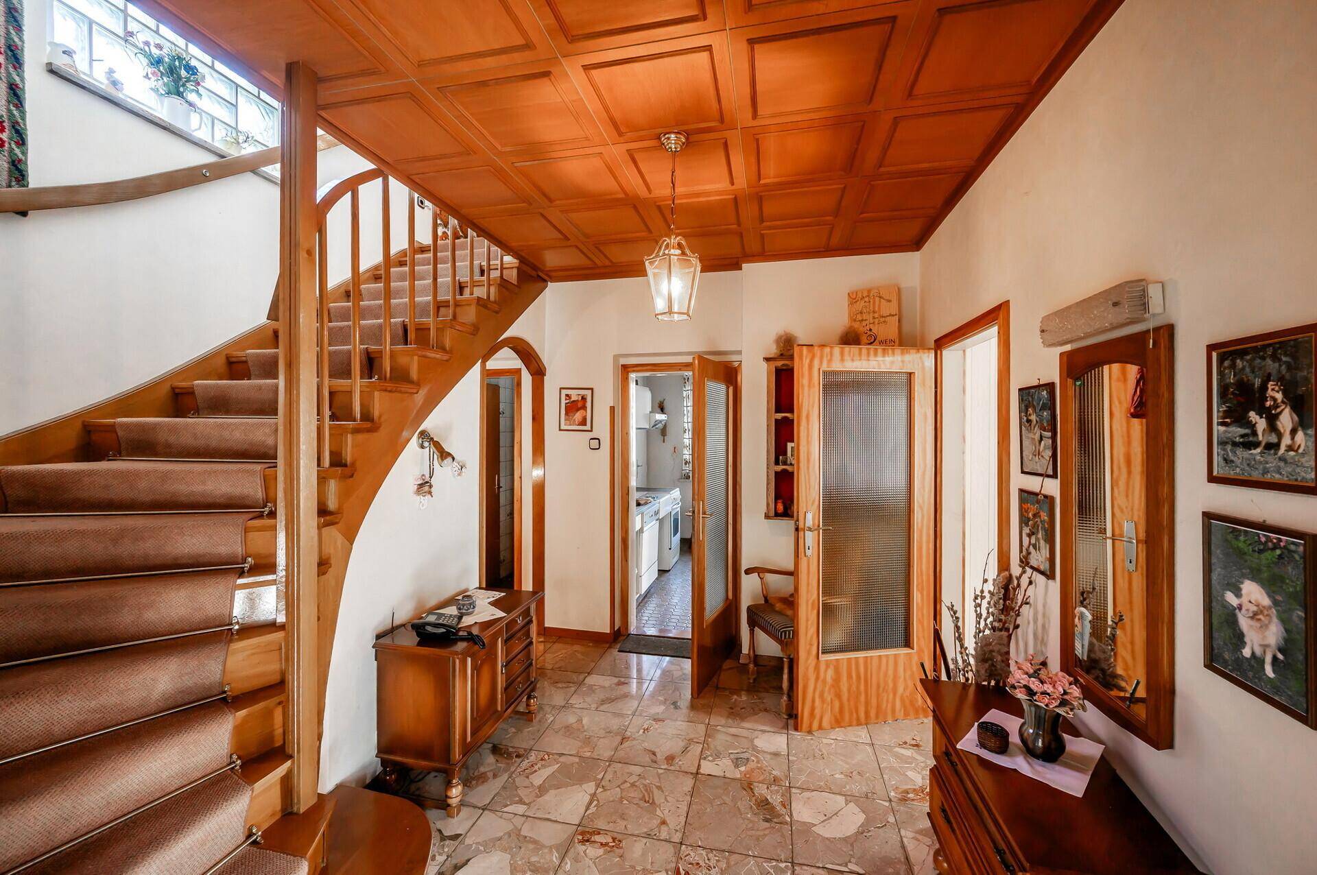 Geräumiger Flur mit Holztreppe, gemustertem Fliesenboden und einer Kassettendecke aus Holz.