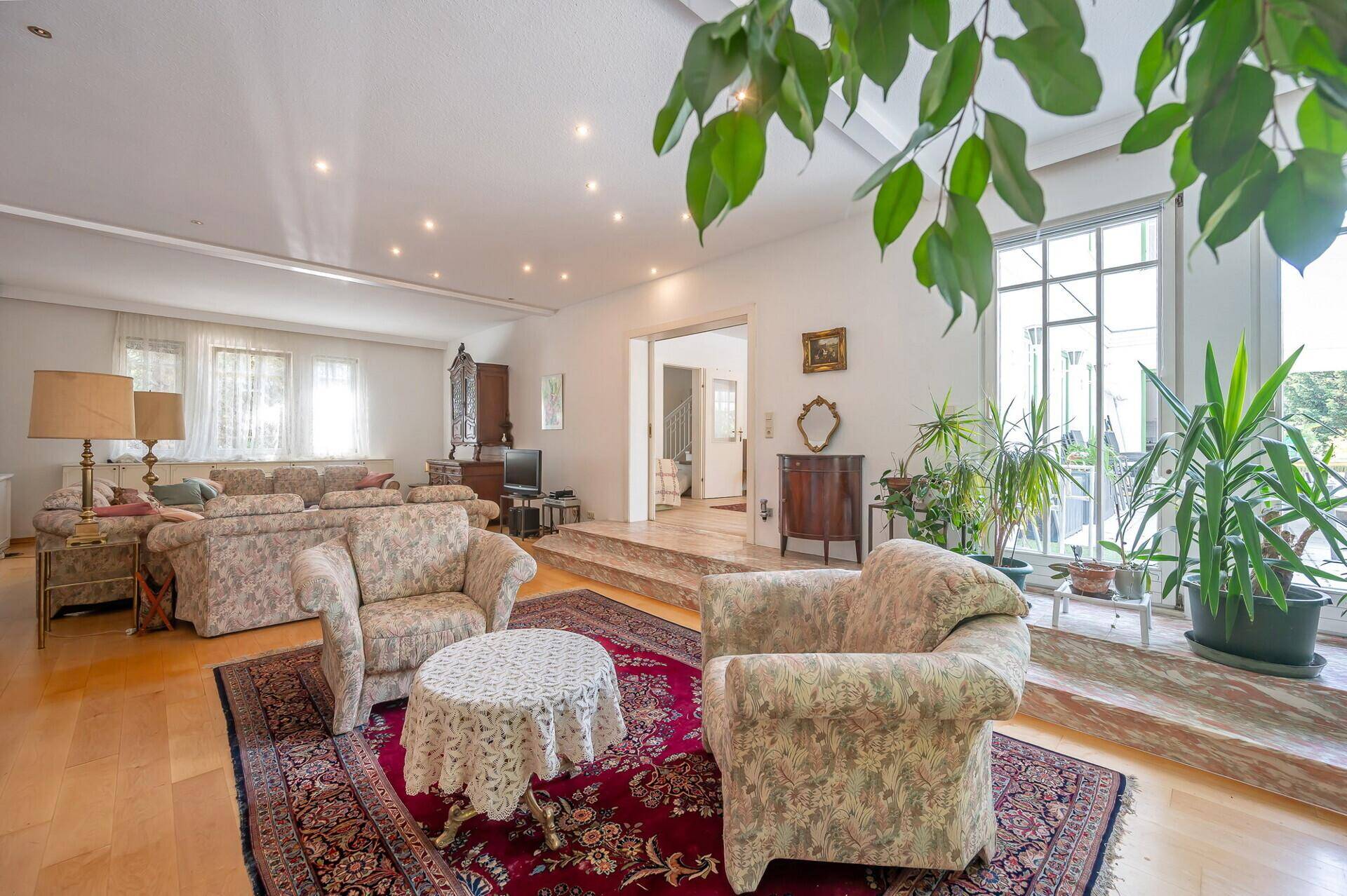 Großes Wohnzimmer mit Parkettboden, vielen Pflanzen und Blick in den Garten.