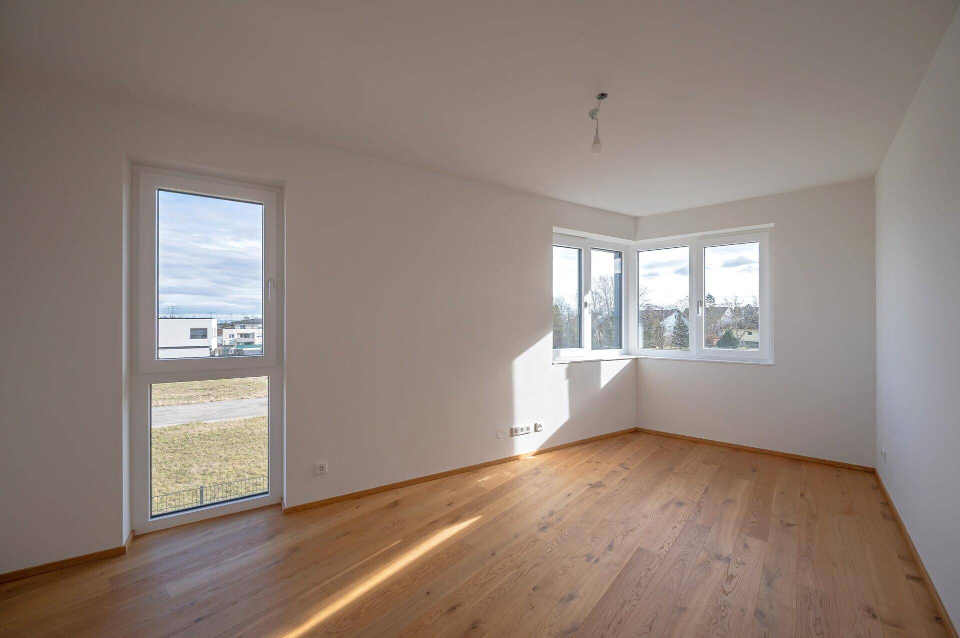 Helles Schlafzimmer mit Holzboden und großen Fenstern, die viel Licht spenden.