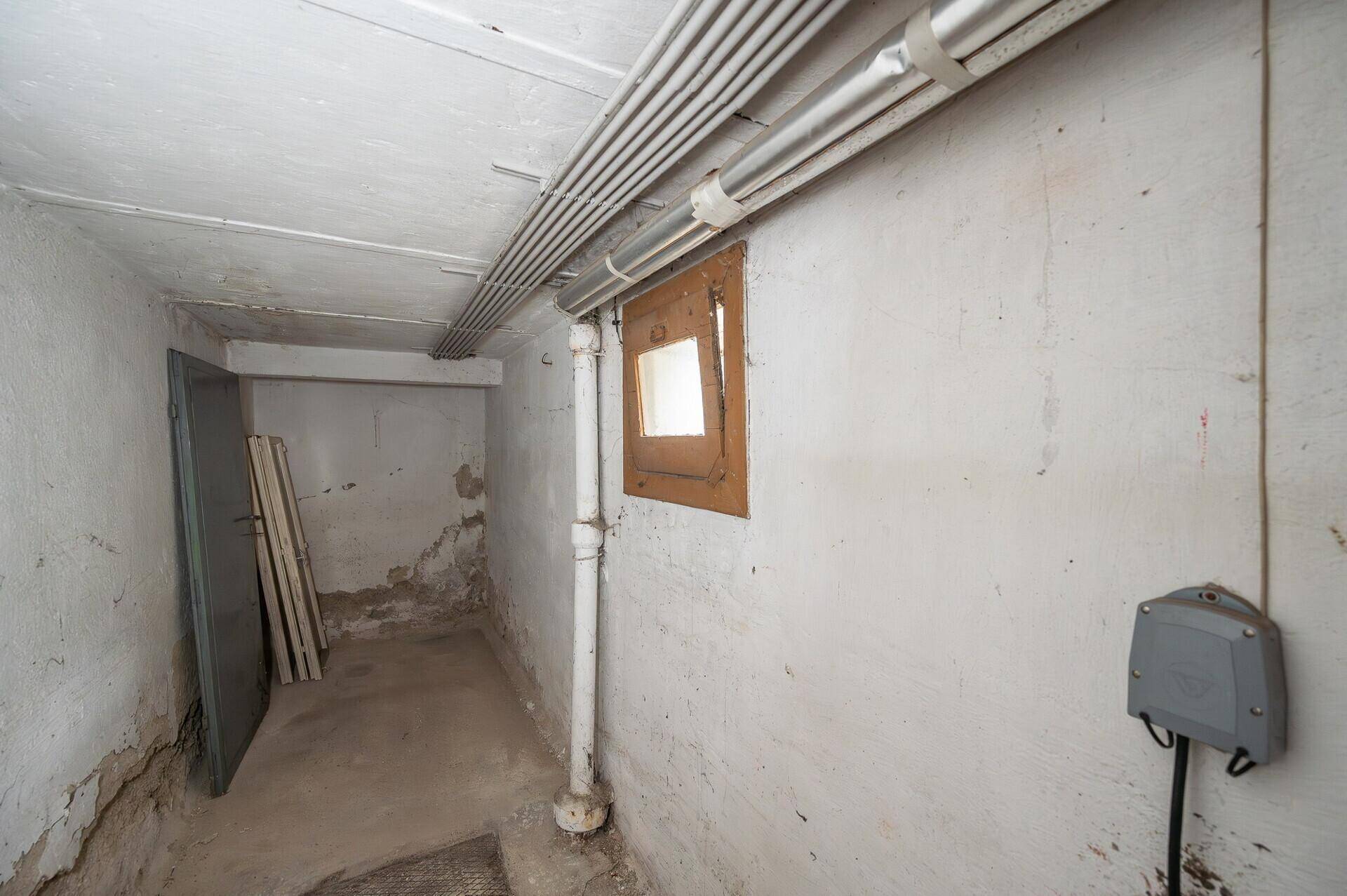 Schmaler Kellergang mit Rohren und kleinem Fenster, bietet zusätzlichen Stauraum.