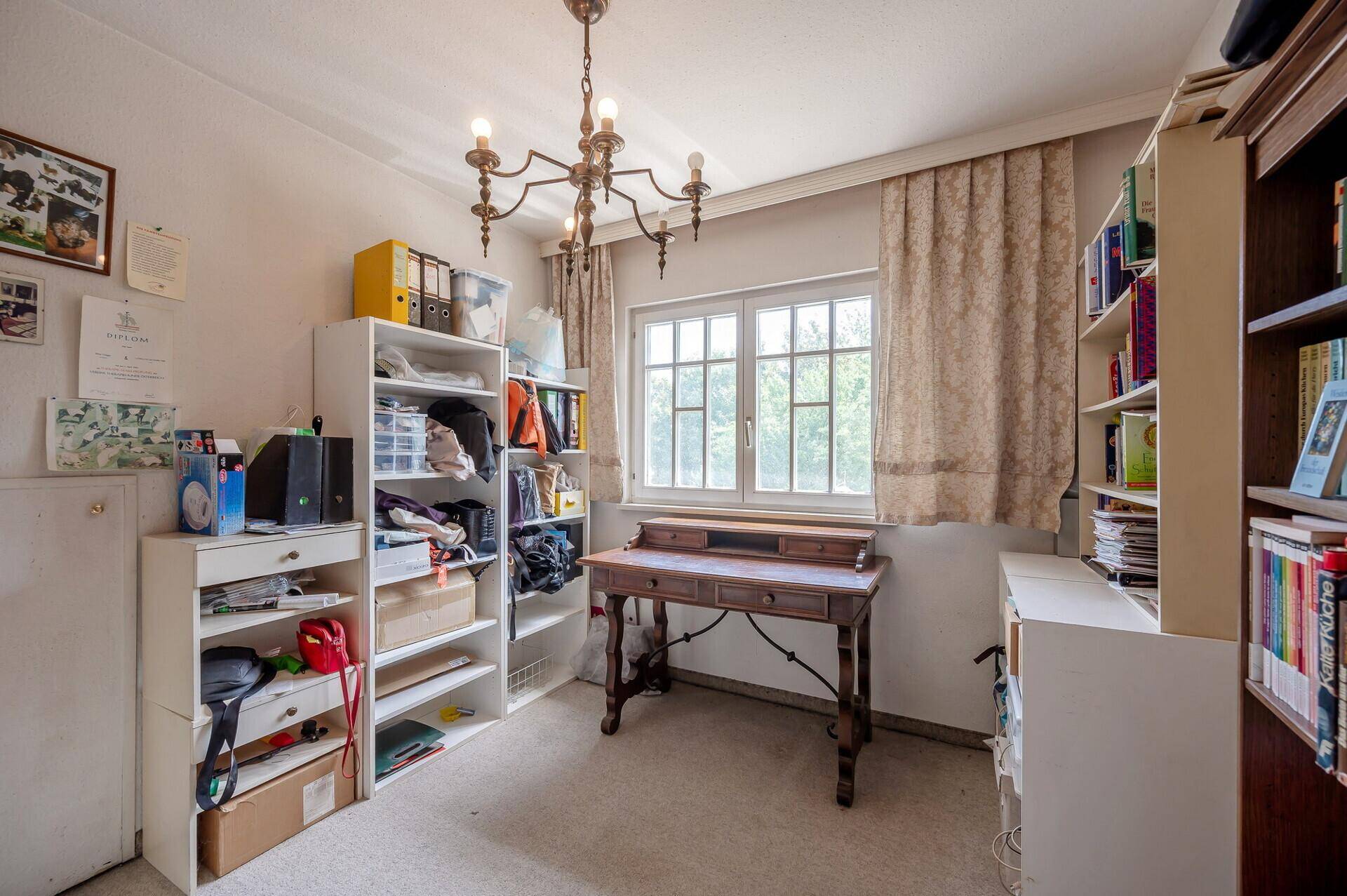 Arbeitszimmer mit Schreibtisch, Bücherregalen und Kronleuchter.