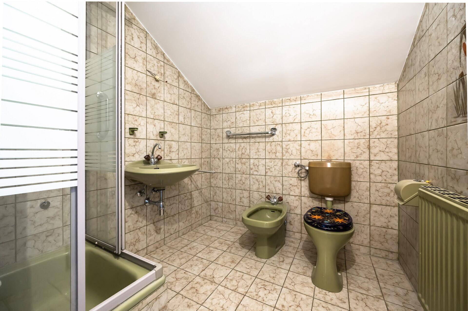 Badezimmer mit beigefarbenen Fliesen, Dusche, WC und Bidet in älterem Stil.