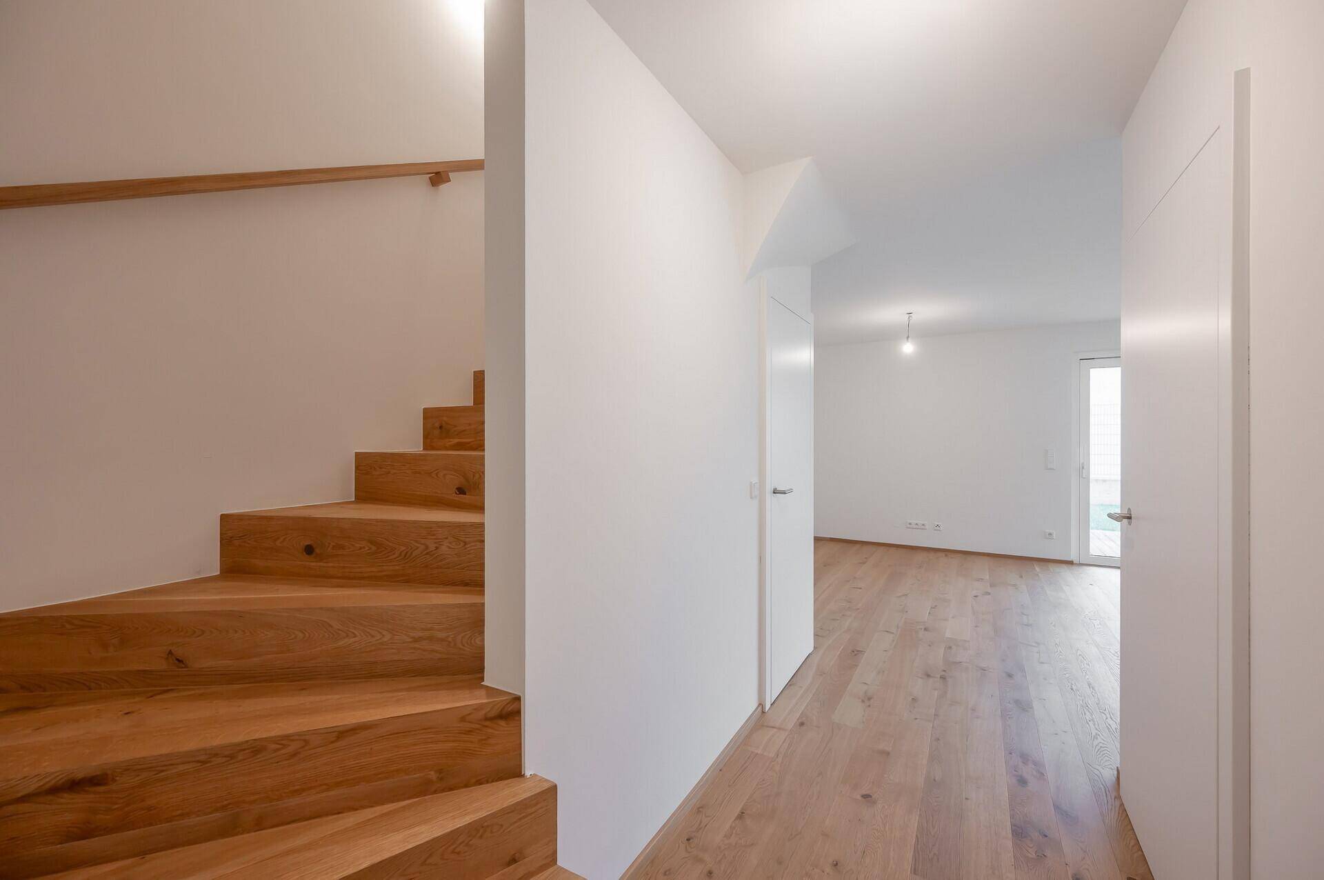 Heller Flur mit Holztreppe und Zugang zu den oberen Etagen.