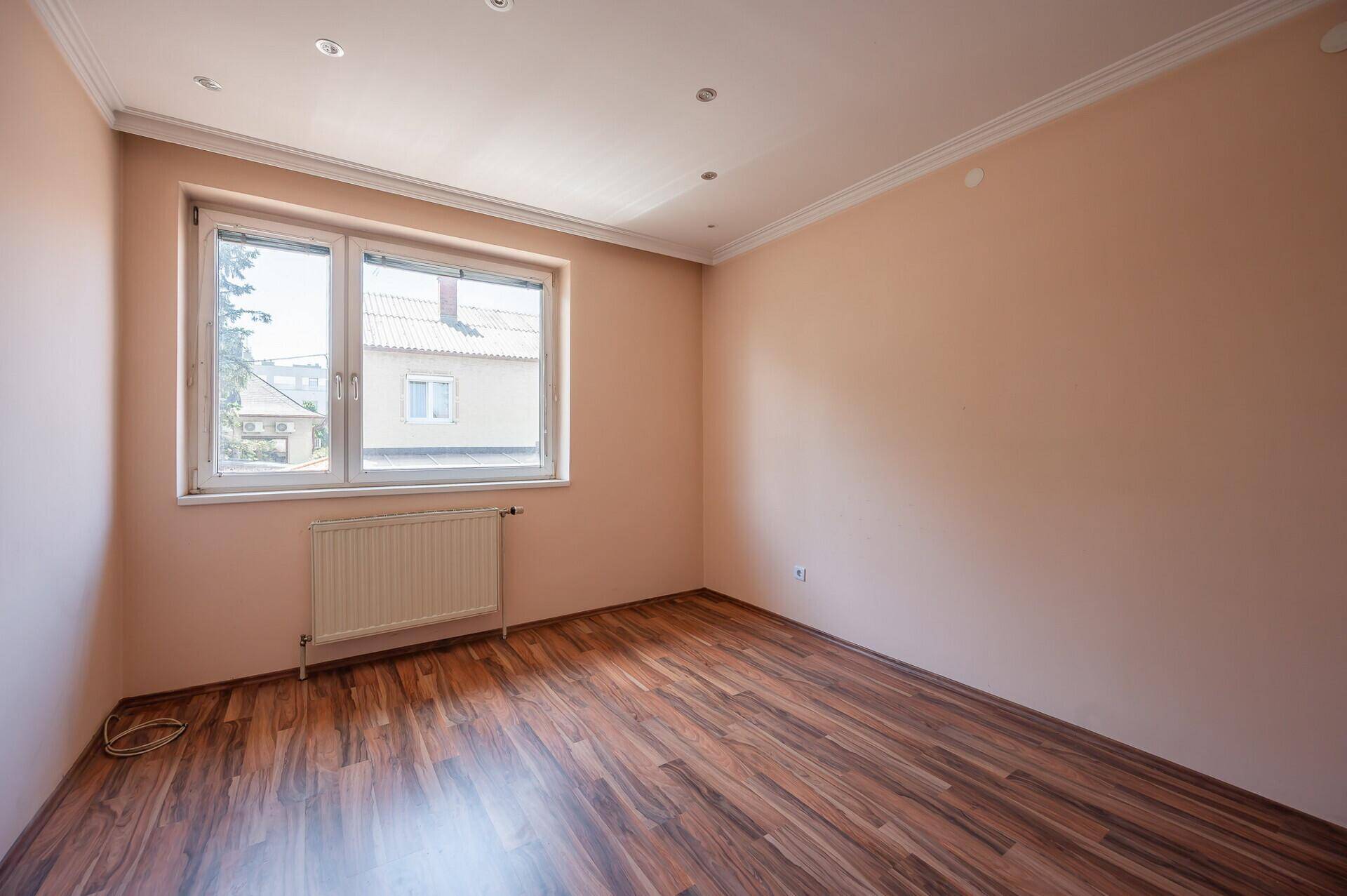 Helles Schlafzimmer mit Laminatboden, beigen Wänden und einem großen Fenster.