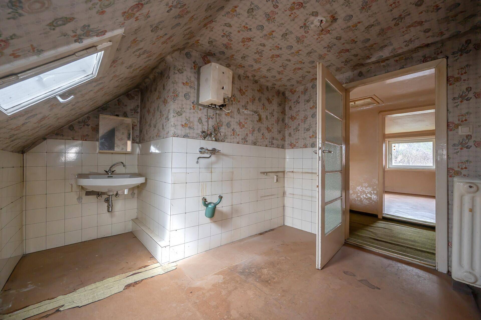Dachgeschoss-Badezimmer mit Waschbecken, Fliesen und Dachfenster, sanierungsbedürftig.