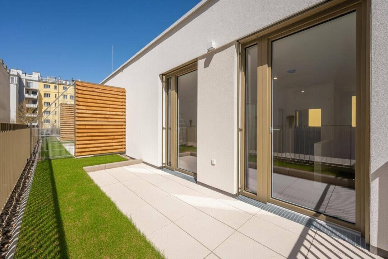 Sonnige Terrasse mit Kunstrasen und großen Schiebetüren zum Innenbereich.