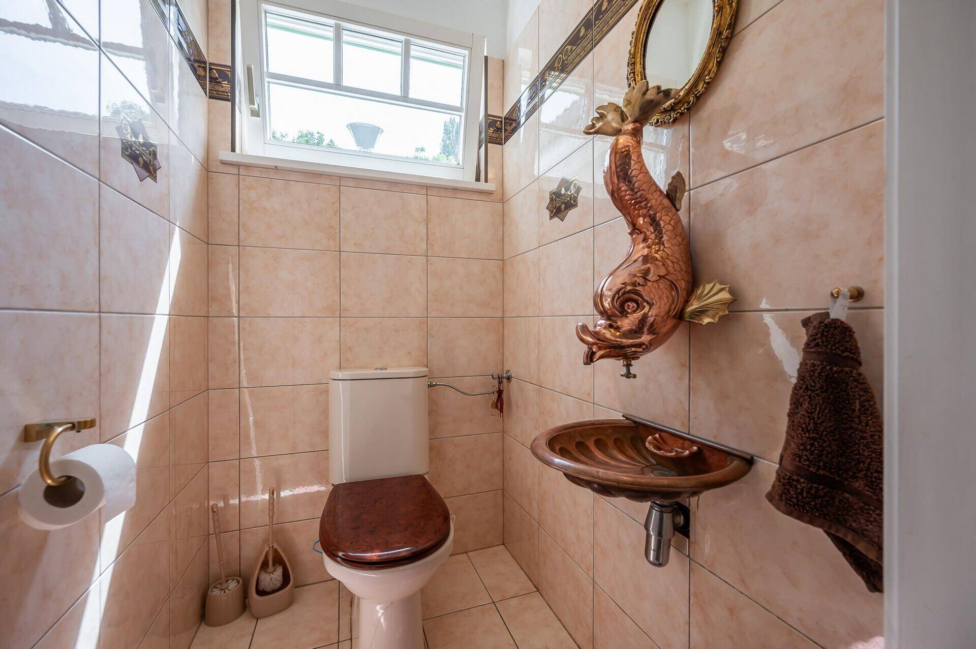 Kleines Gäste-WC mit beigefarbenen Fliesen, Fenster und dekorativem Waschbecken.