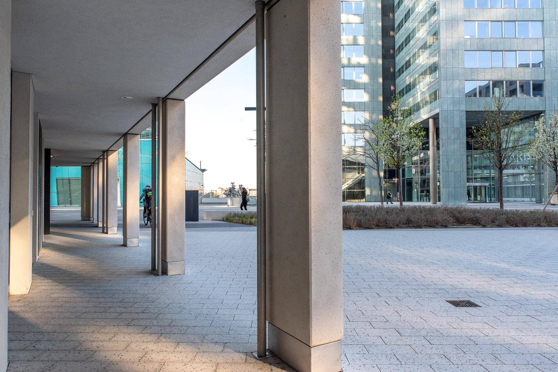Überdachter Gehweg mit Säulen und Blick auf moderne Hochhäuser in der Ferne.