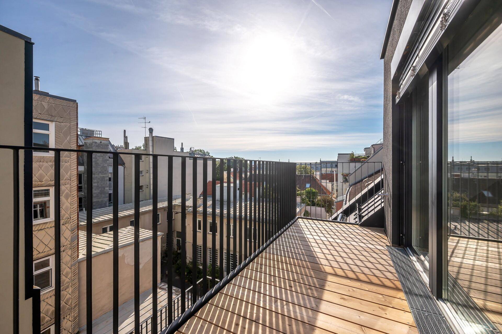 Moderner Balkon mit Holzbelag und schwarzem Metallgeländer, bietet einen Blick auf die Stadt.