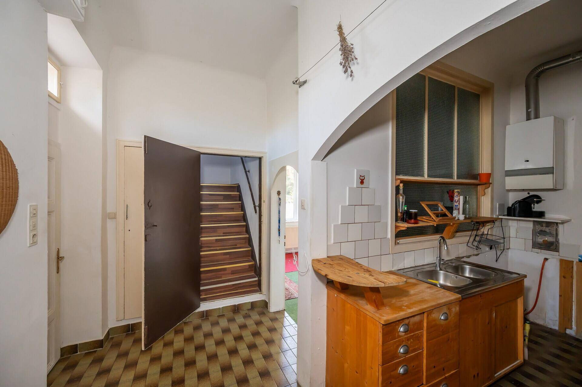 Küche mit Fliesenboden, Spüle und Blick auf die Holztreppe, renovierungsbedürftig.