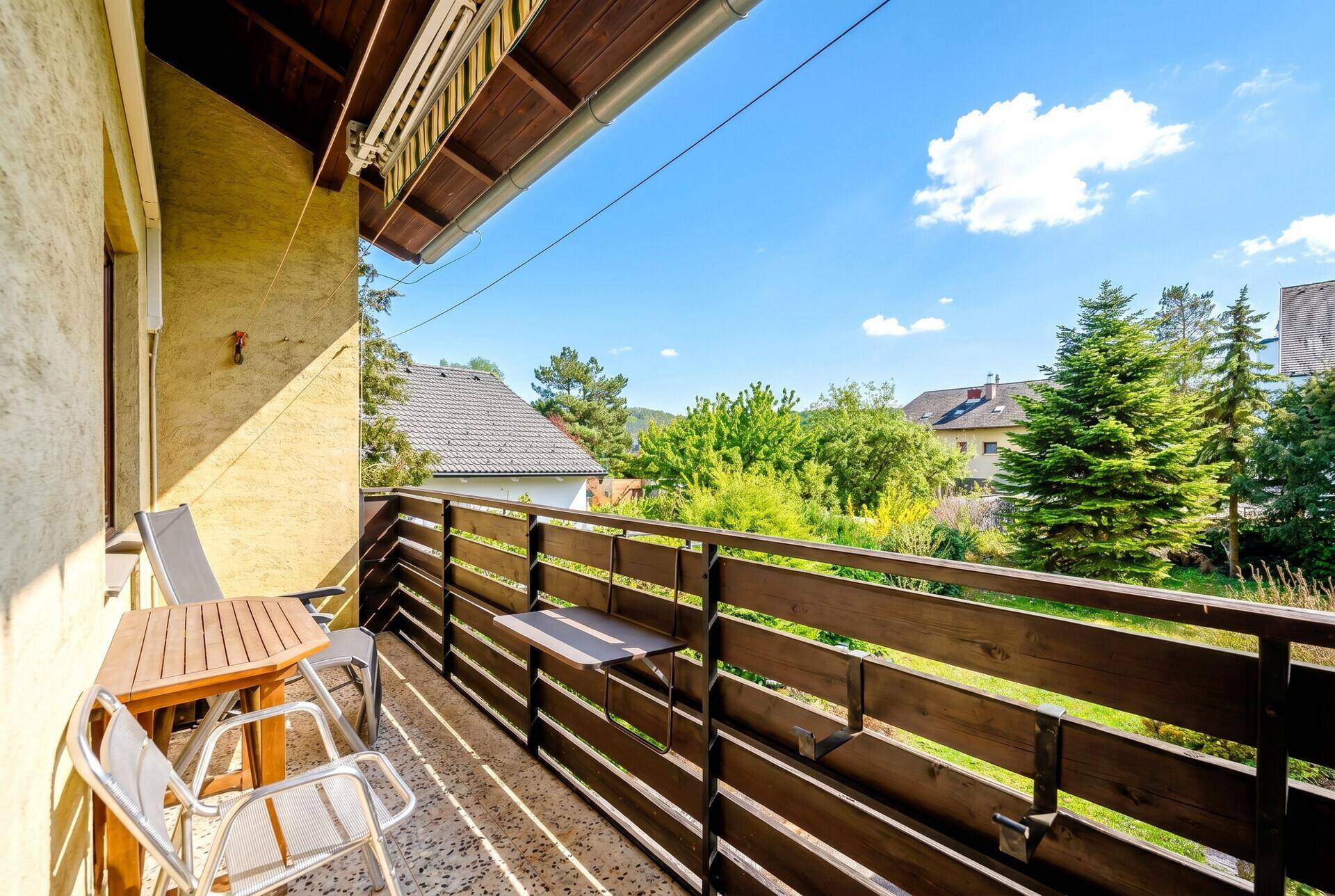 Sonniger Balkon mit Gartenmöbeln und Blick auf die grüne Umgebung und Nachbarhäuser.