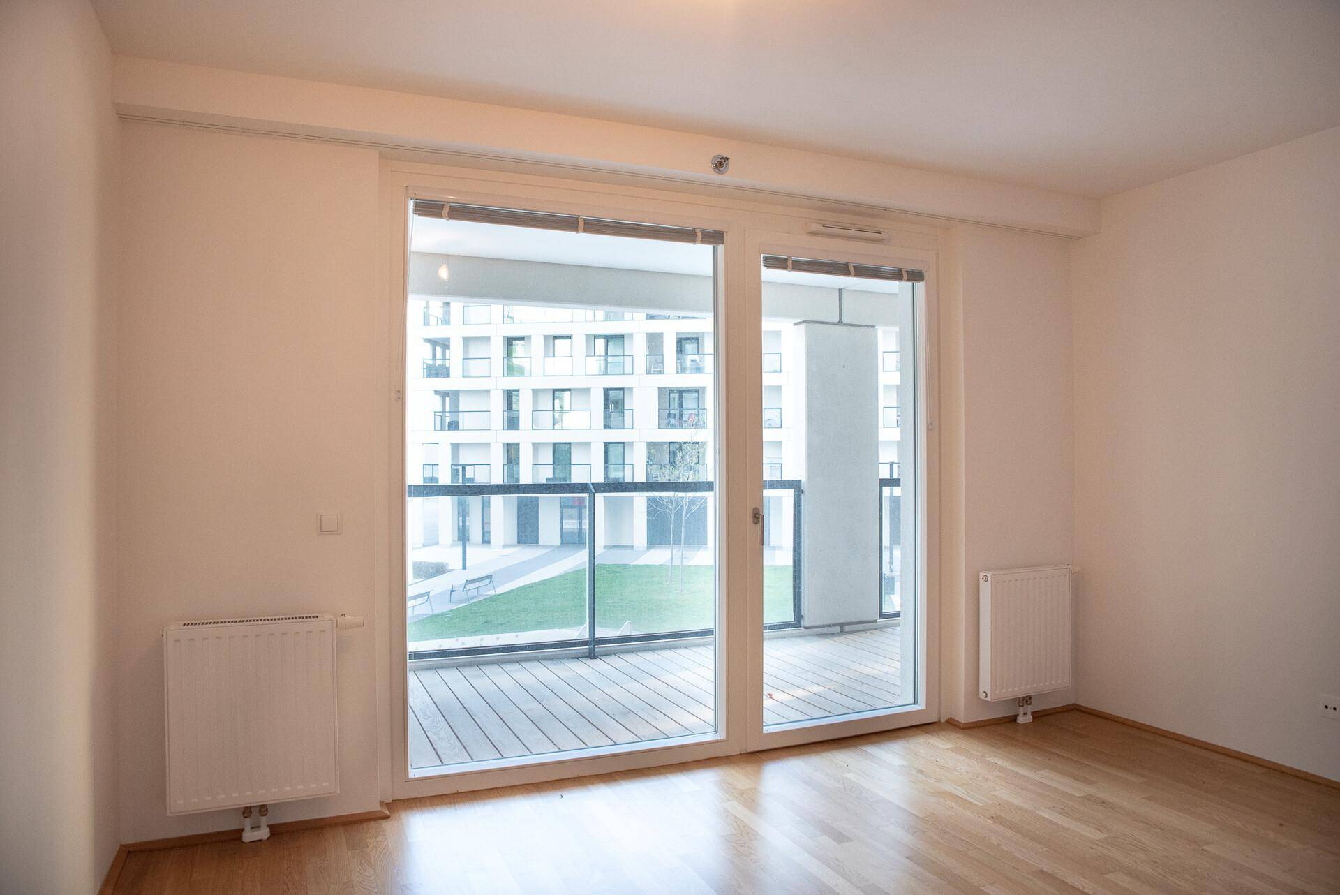 Helles Schlafzimmer mit Holzboden und großem Fenster, das Zugang zu einem Balkon bietet.