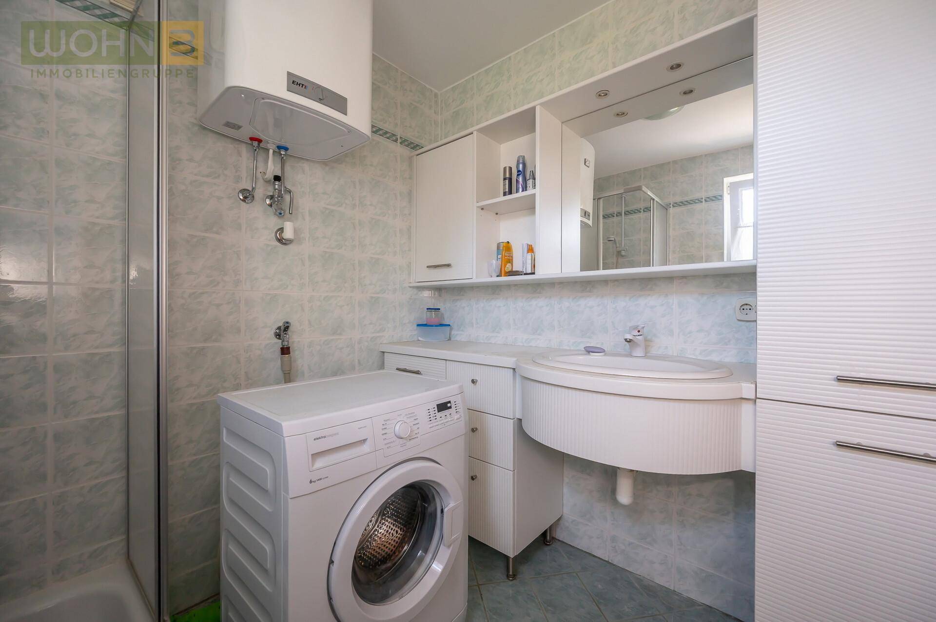 Badezimmer mit Waschbecken, Spiegelschrank, Duschbereich und integrierter Waschmaschine.