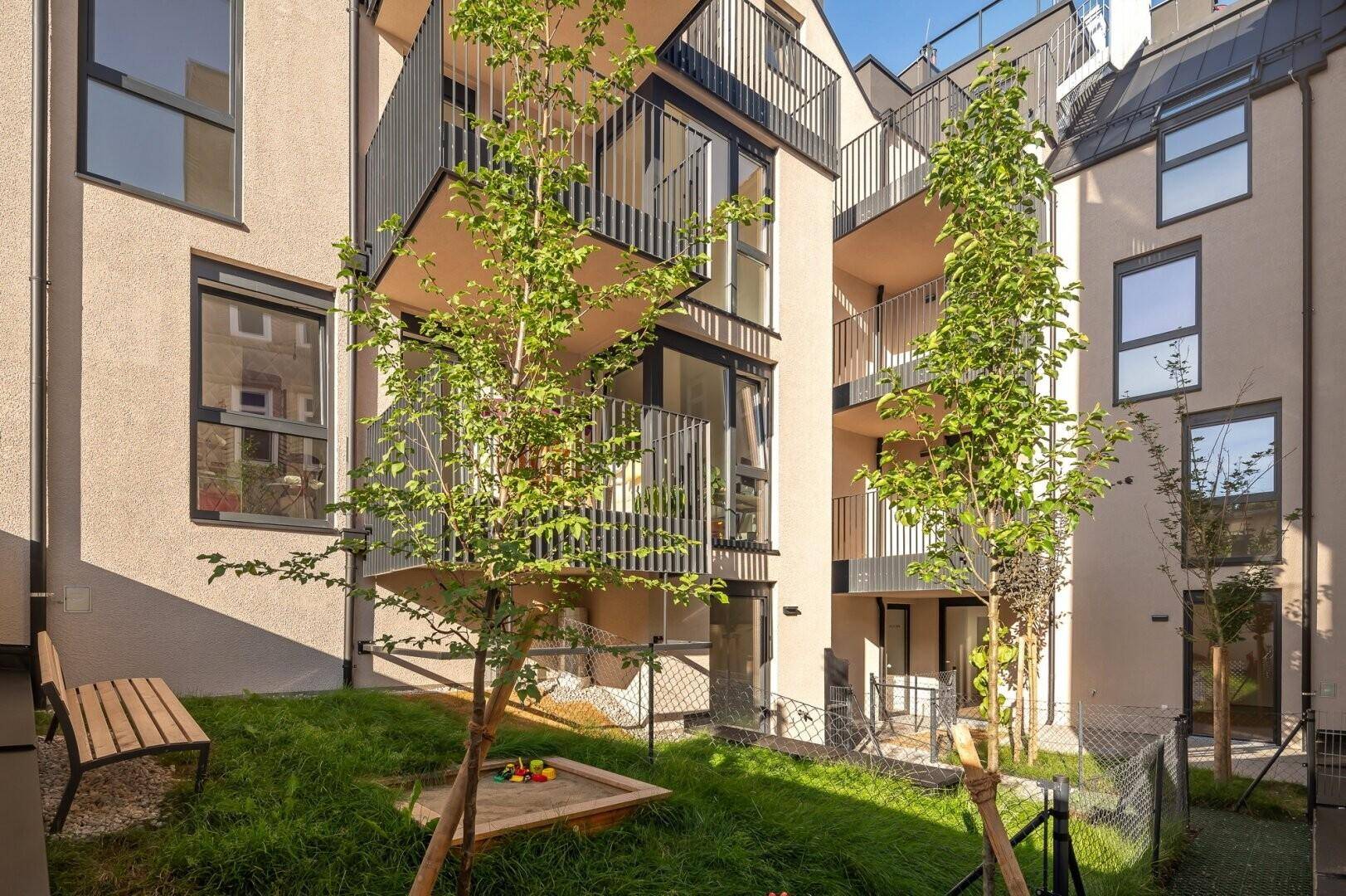 Grüner Innenhof mit Sitzbank und kleinem Sandkasten, umgeben von modernen Gebäuden.