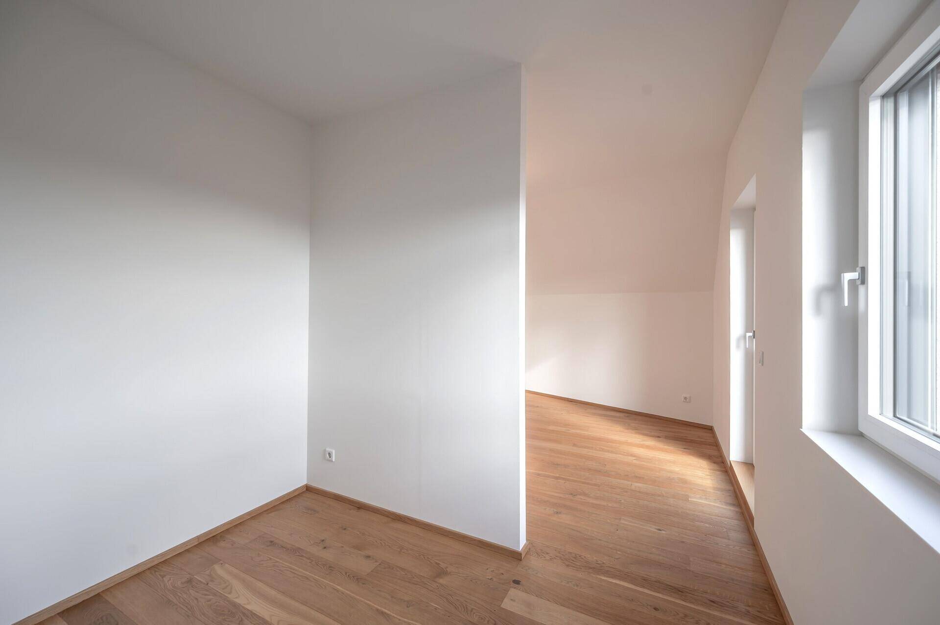 Helles Schlafzimmer im Dachgeschoss mit Holzboden und schrägen Wänden.