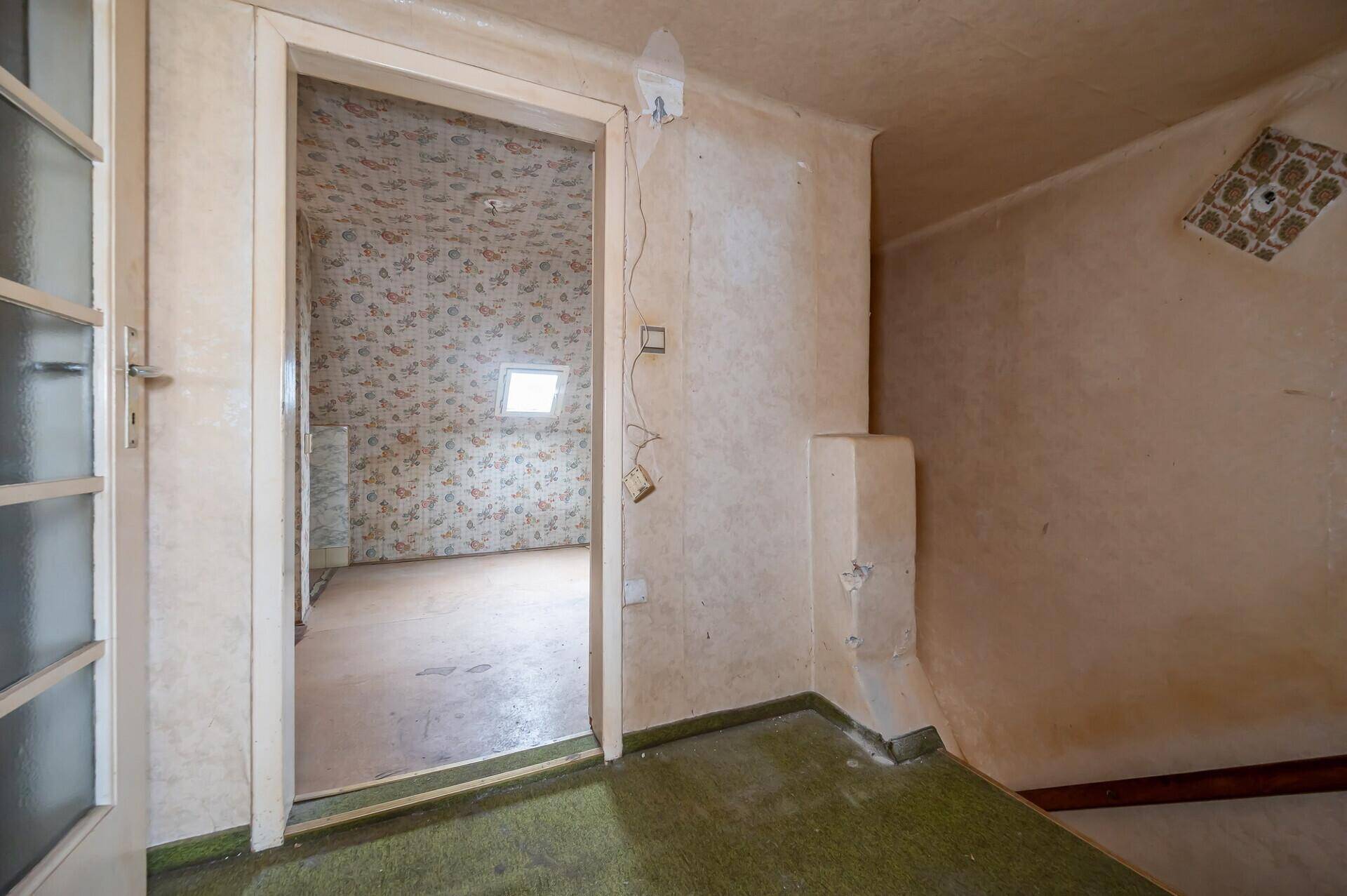 Renovierungsbedürftiger Raum mit alter Tapete und Blick in ein weiteres Zimmer.