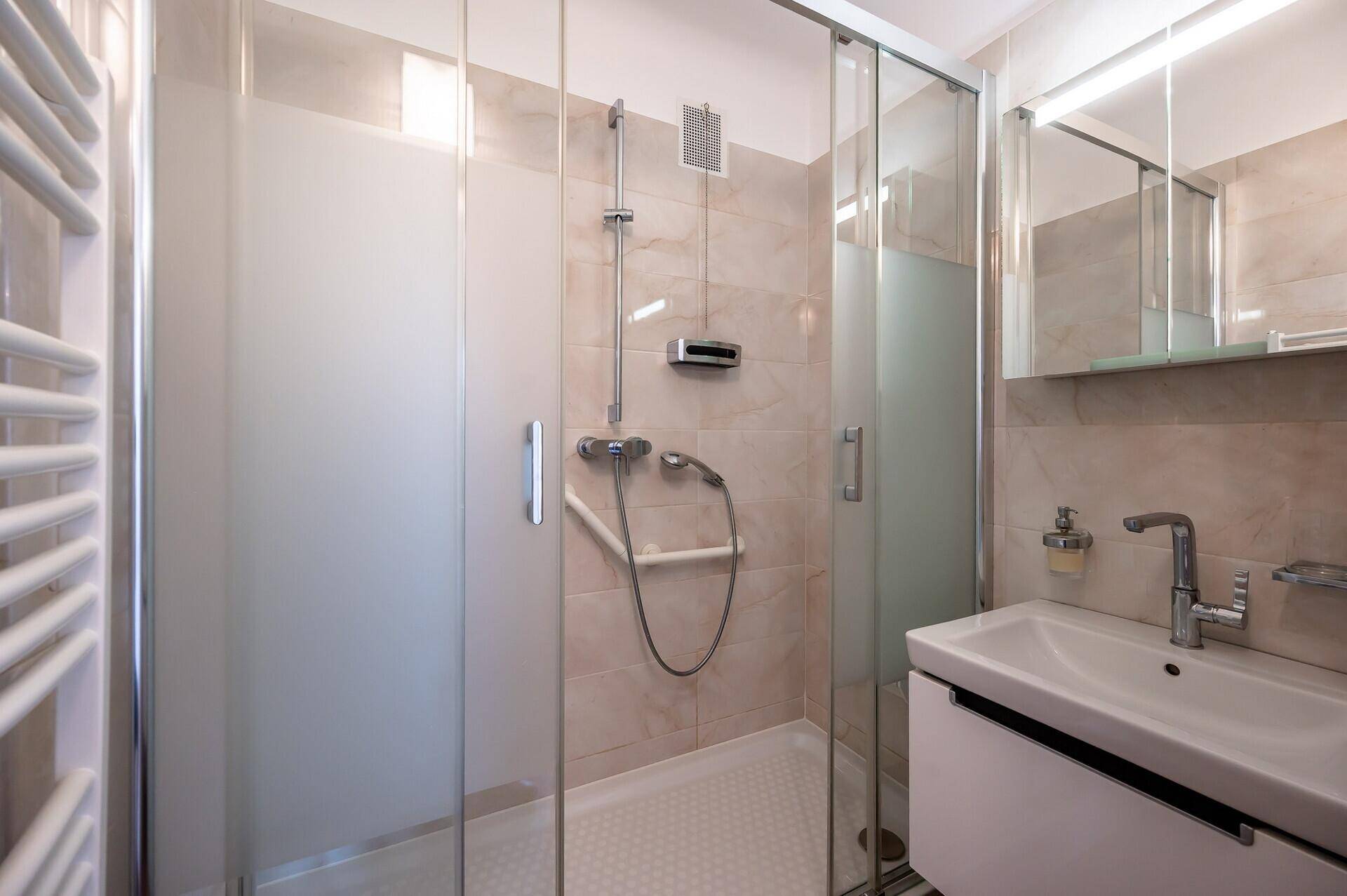 Modernes Badezimmer mit Duschkabine, Waschbecken und beheiztem Handtuchhalter.