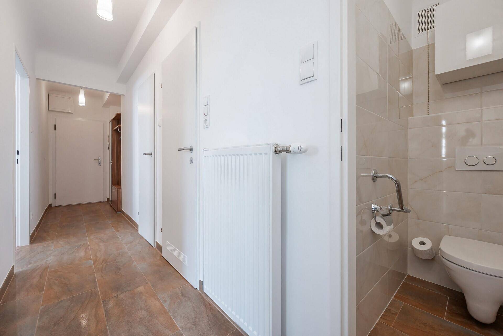 Separates WC mit Wand-WC, Haltegriffen und Fliesen an Wänden und Boden.