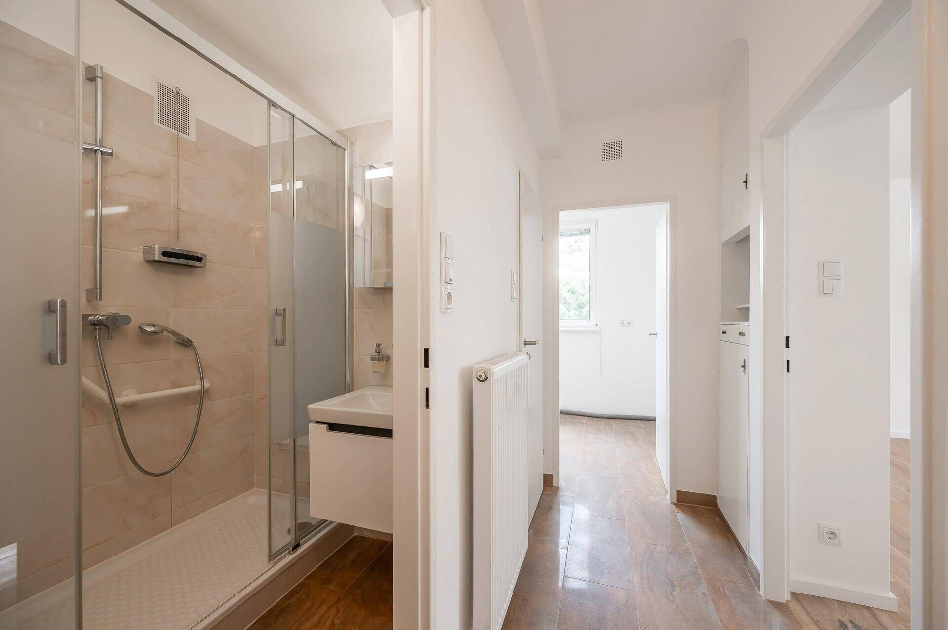 Flur mit Zugang zum Badezimmer und Blick in einen weiteren Raum, alles hell gefliest.