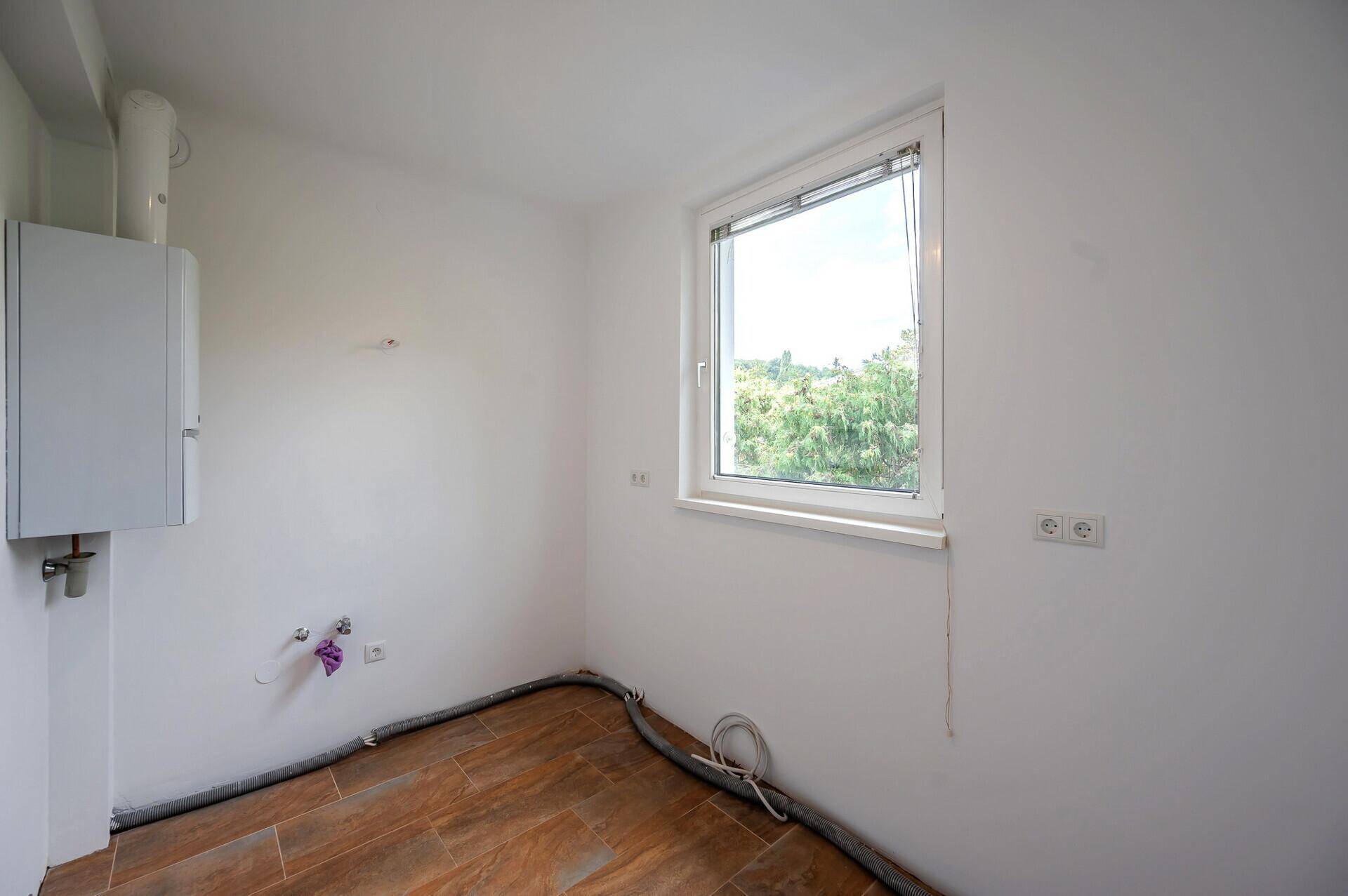 Kleiner Raum mit Heizungsanlage, Anschlüssen und einem Fenster, ideal als Abstellraum.