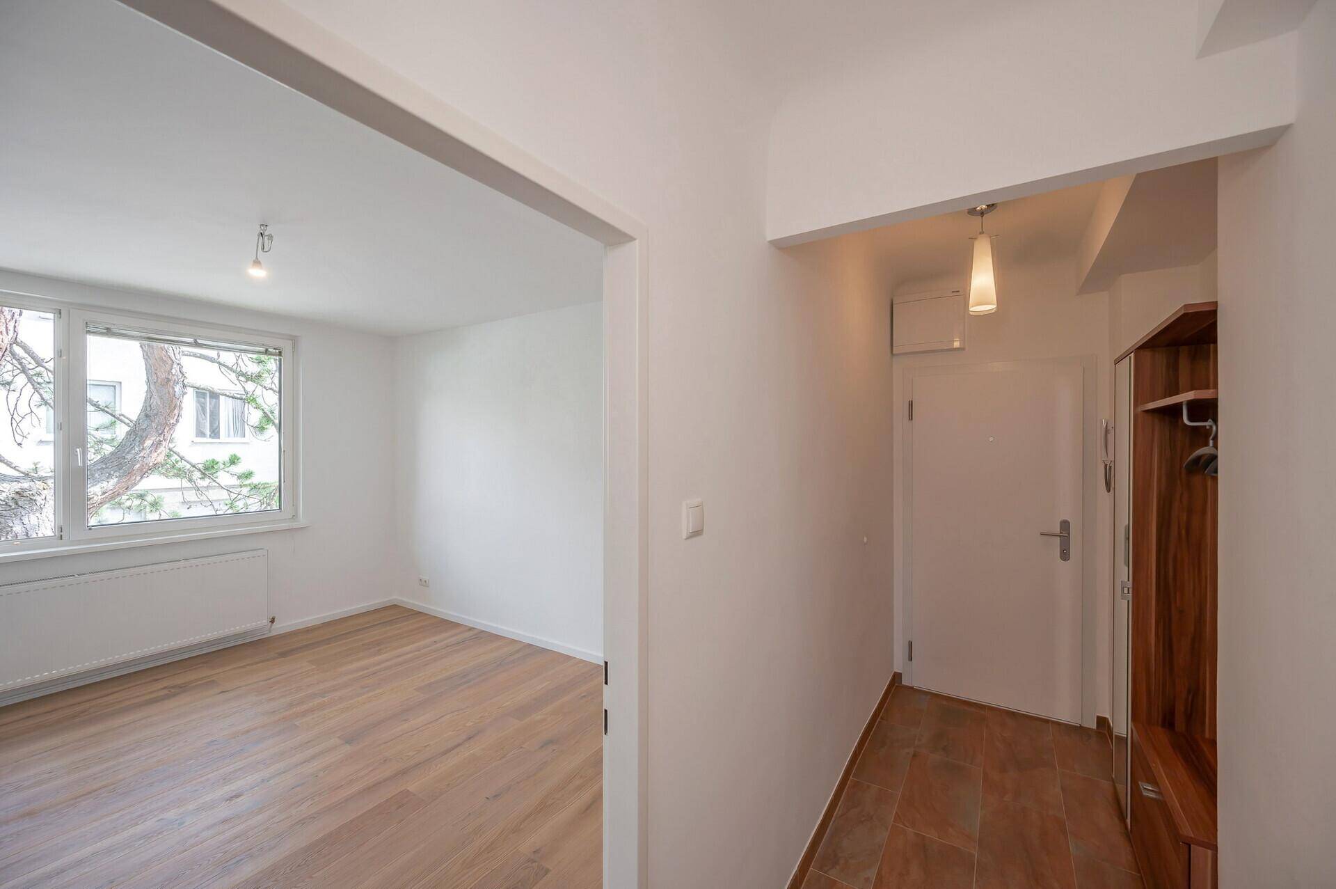 Eingangsbereich mit Garderobe und Blick in ein helles Zimmer mit Holzboden.