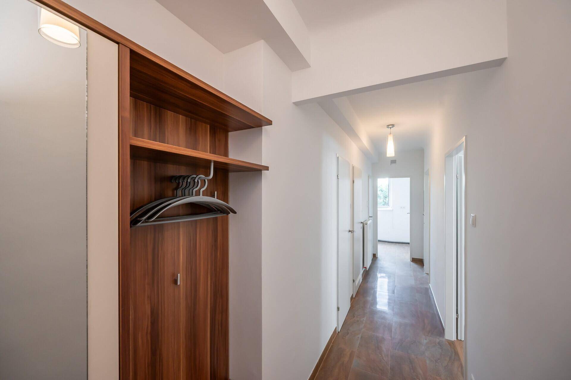 Langer Flur mit Holzgarderobe und Fliesenboden, der zu weiteren Räumen führt.