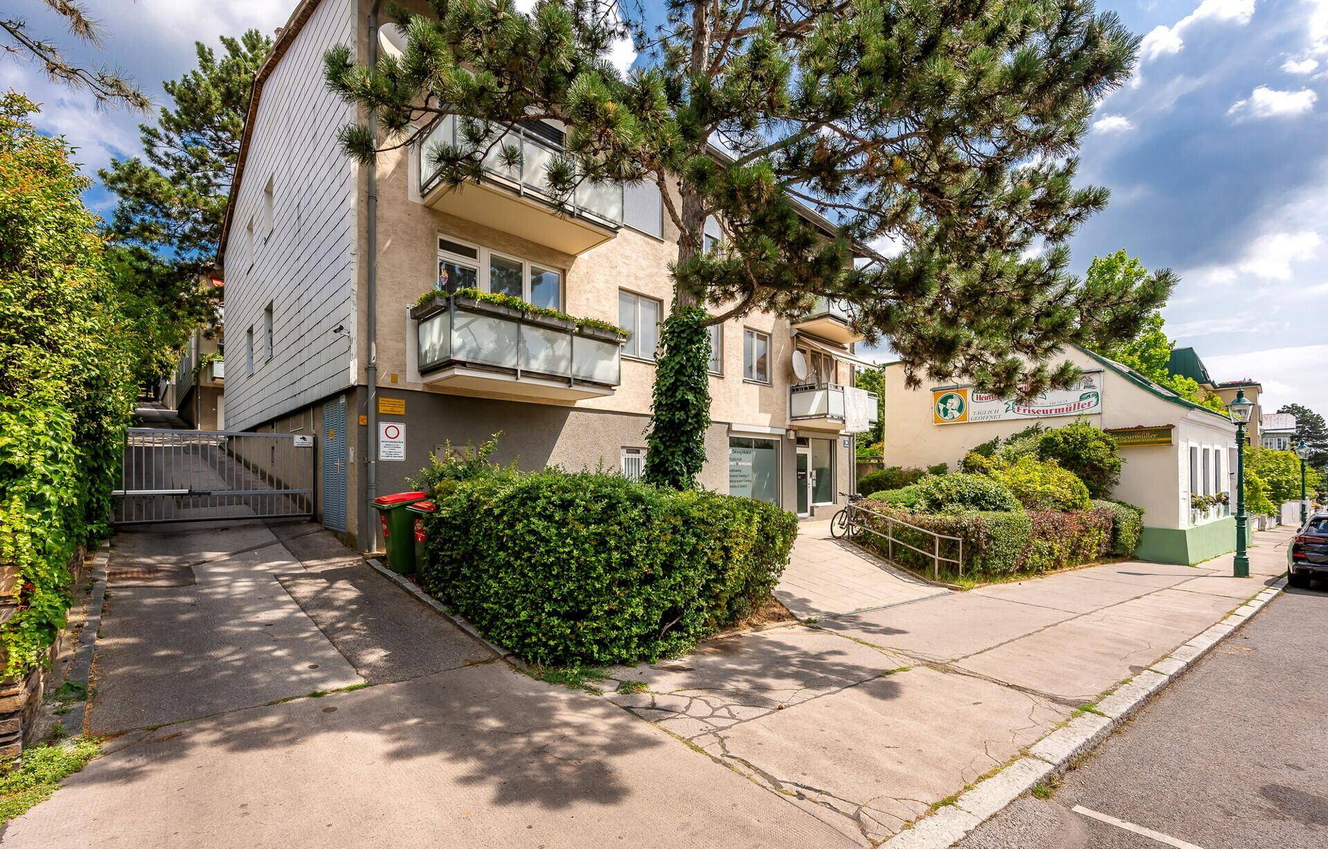 Mehrfamilienhaus mit Balkonen und einer Zufahrt, umgeben von Bäumen und Grünflächen.